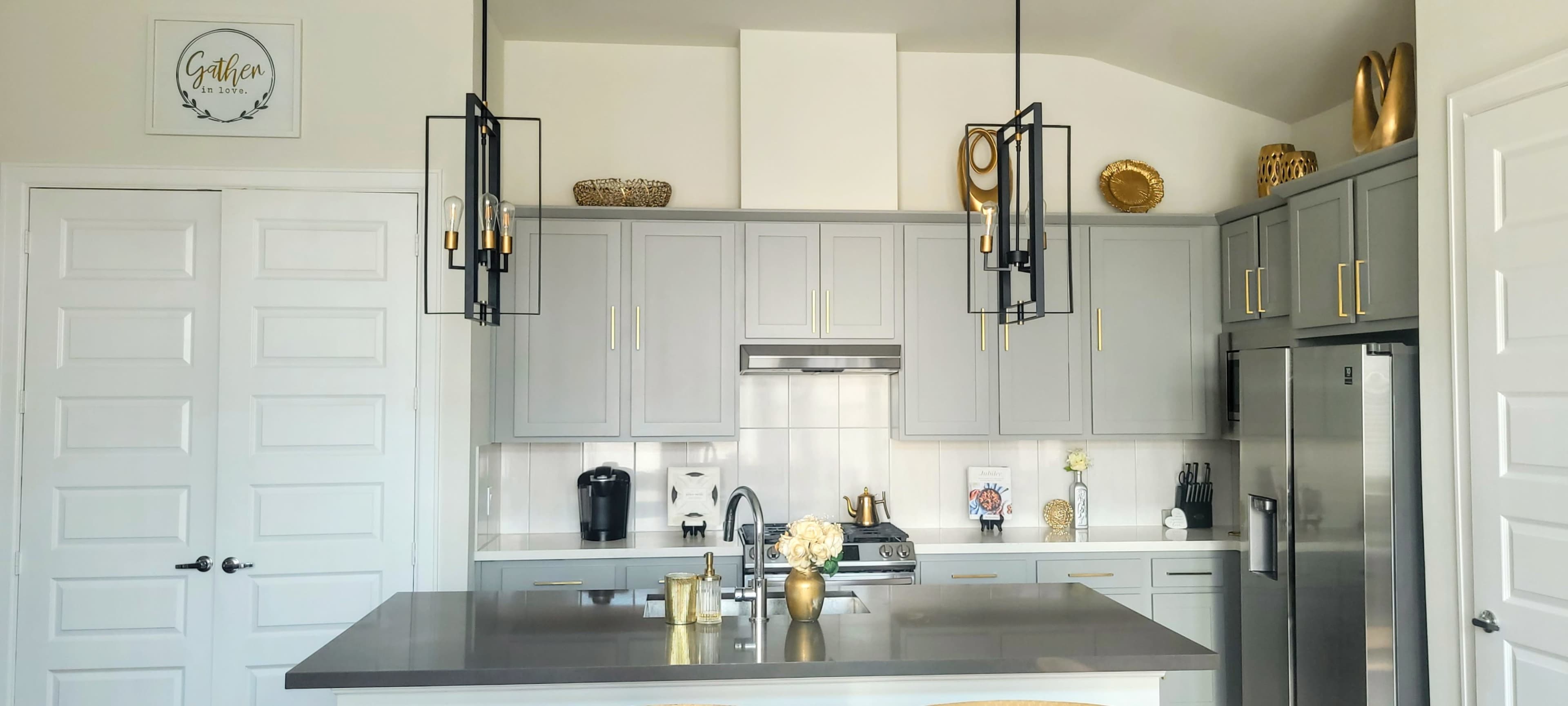 A modern kitchen with gray cabinetry, a large island with a silver countertop, and pendant lights hanging above.