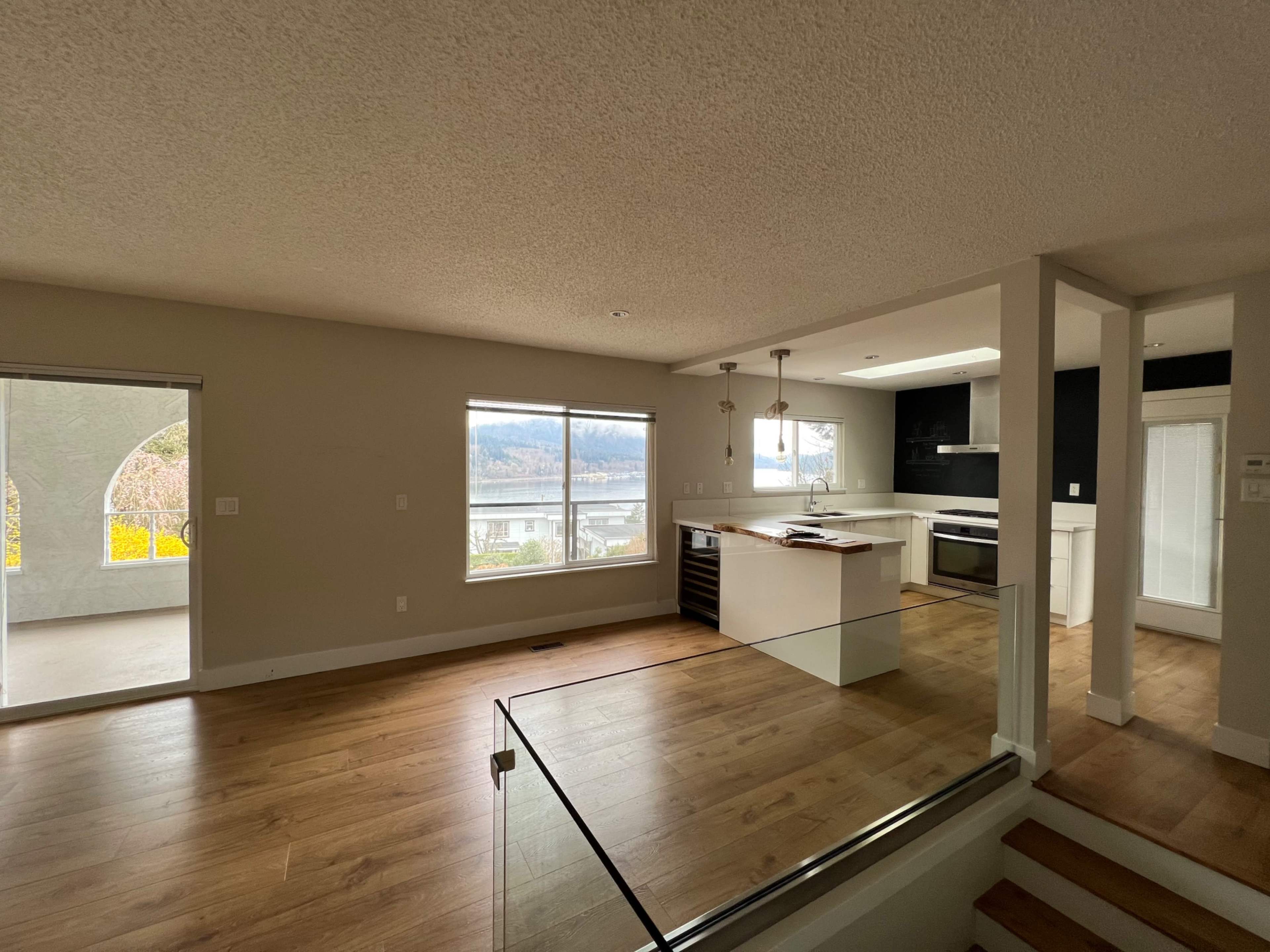 An open-concept living space with a kitchen and dining area, featuring large windows and a light hardwood floor.