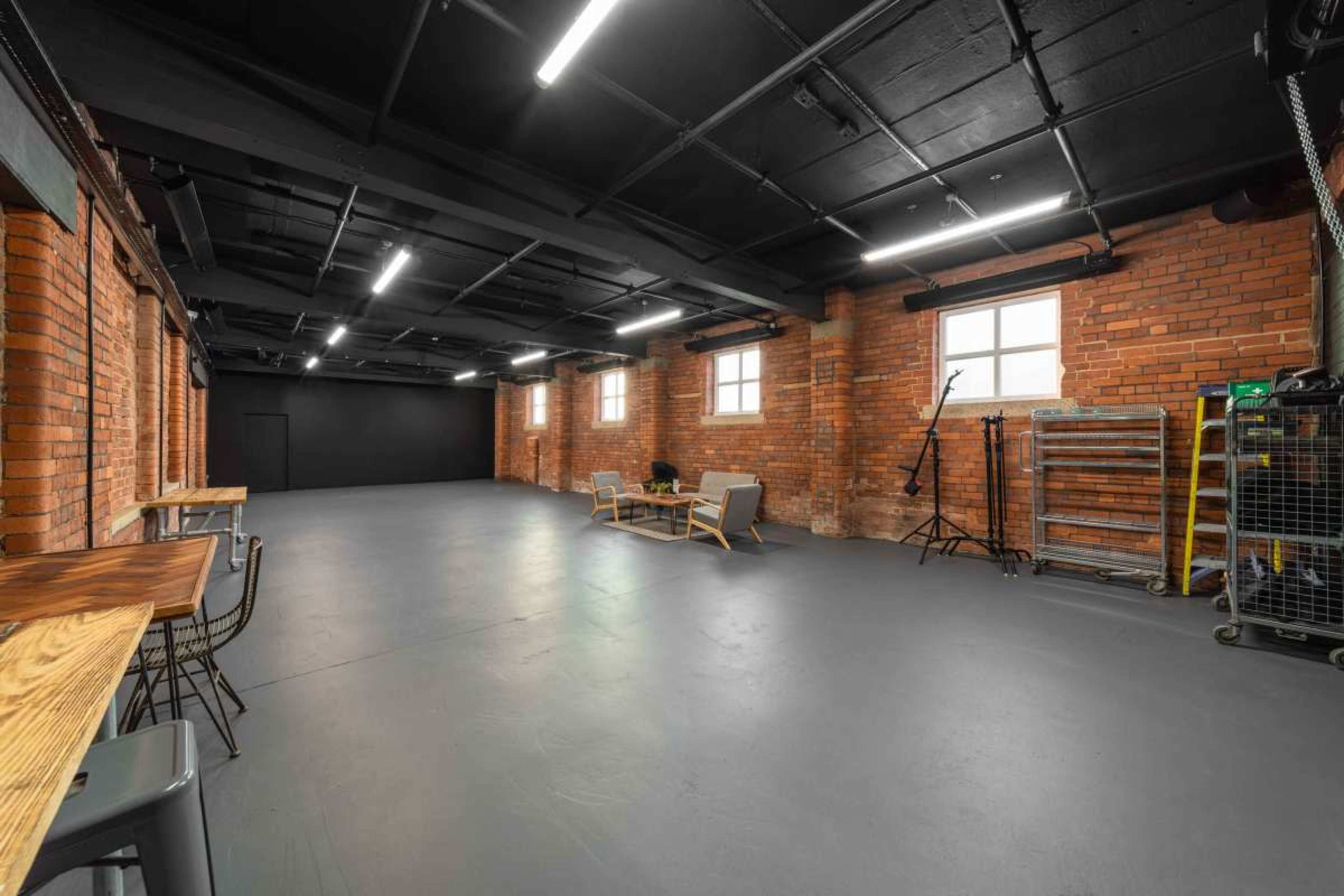 The image shows an industrial-style room with exposed brick walls, polished concrete flooring, and minimal furniture, including a small seating area and a bar counter.