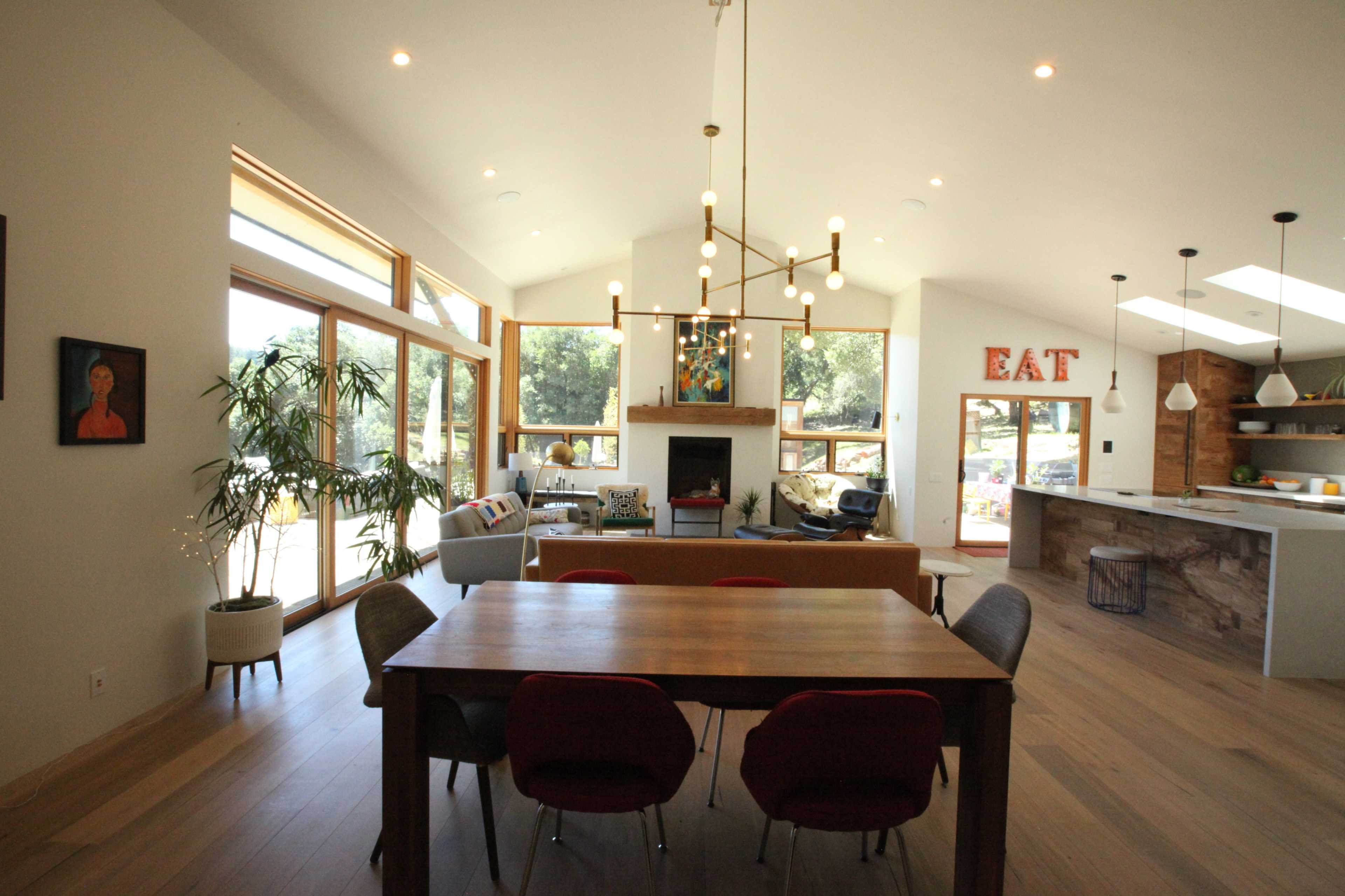 A modern dining area with a wooden table surrounded by chairs, overlooking a spacious living room with large windows and a fireplace.