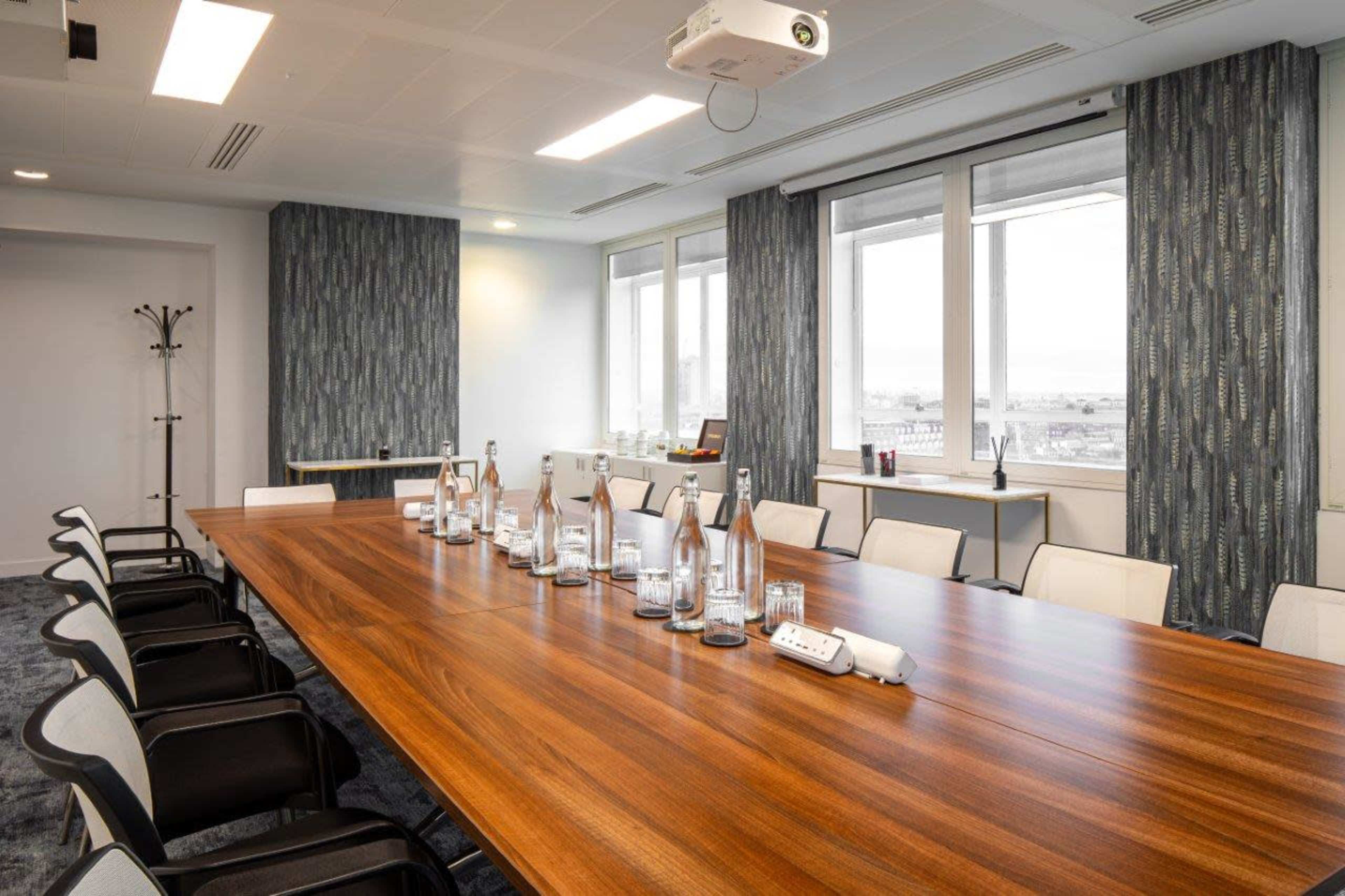 A modern conference room features a long wooden table surrounded by chairs, with a projector and large windows overlooking a cityscape.