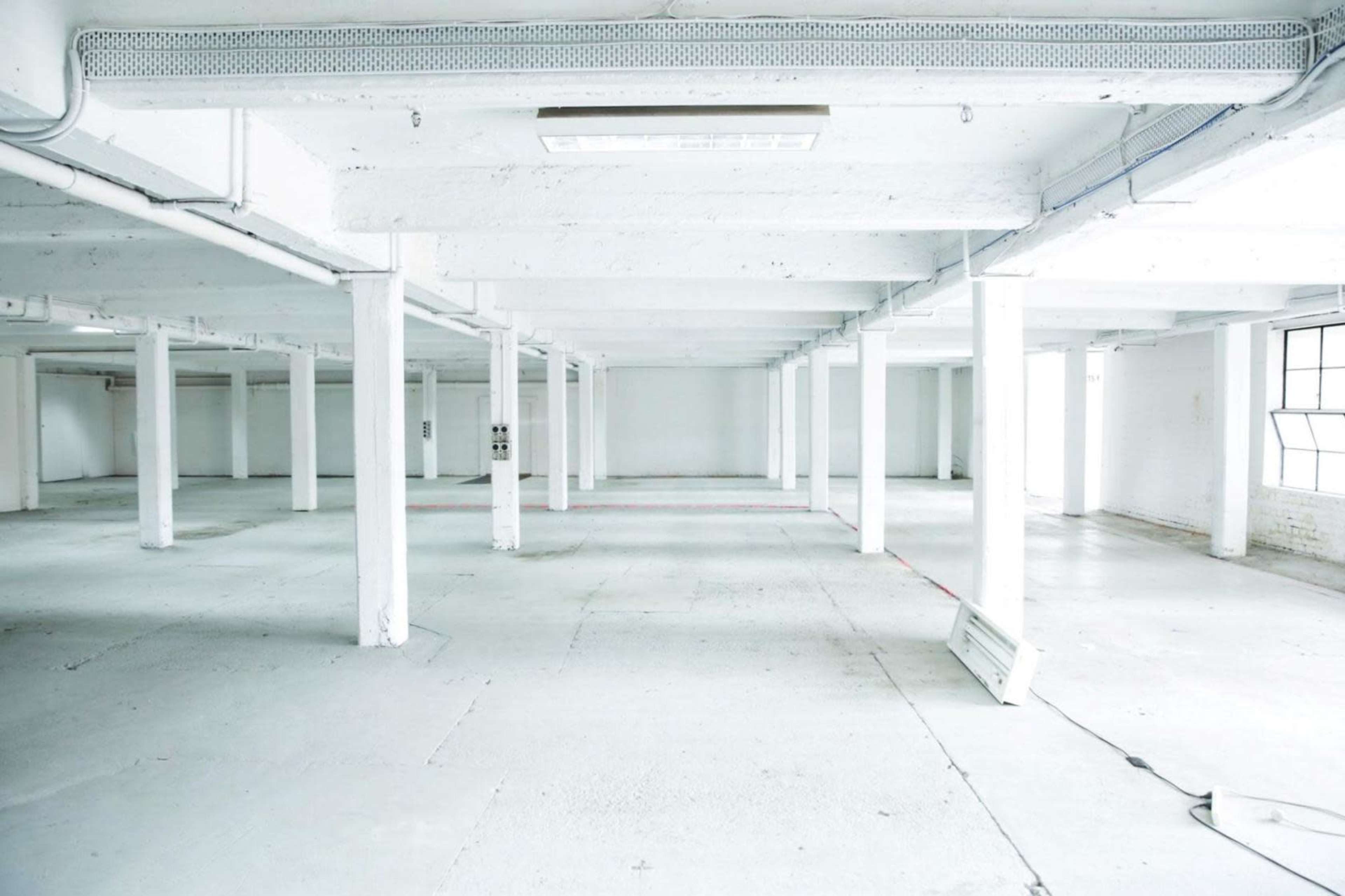 A spacious, empty industrial room with white walls and concrete flooring, supported by several pillars.