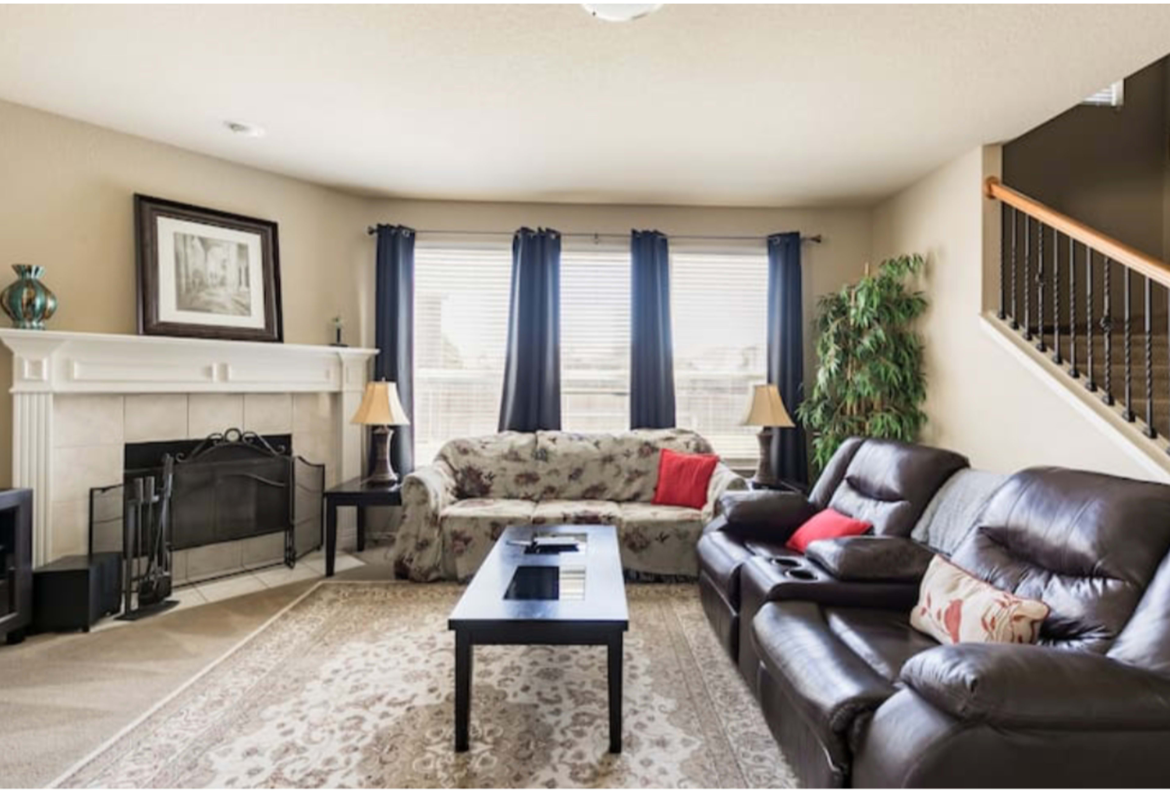 A living room with two sofas, a coffee table, a fireplace, and large windows covered with dark curtains.