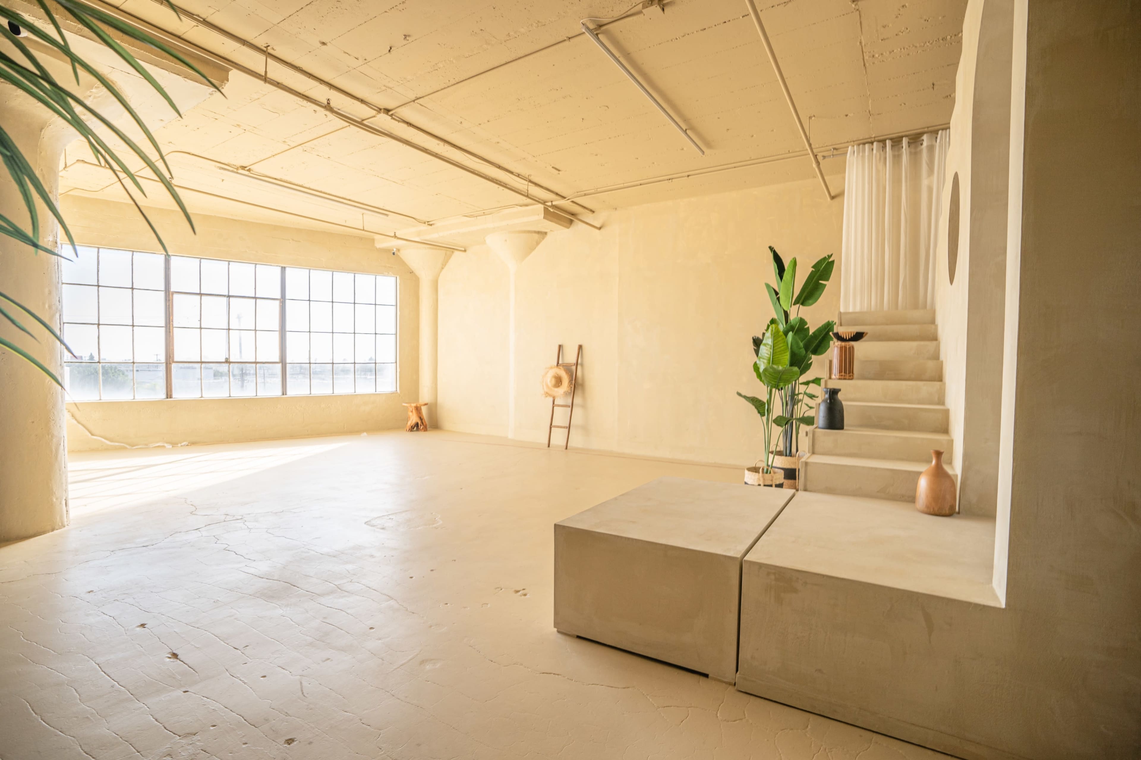 A spacious, minimalist interior with large windows, light-colored walls, and a staircase leading to an upper level.