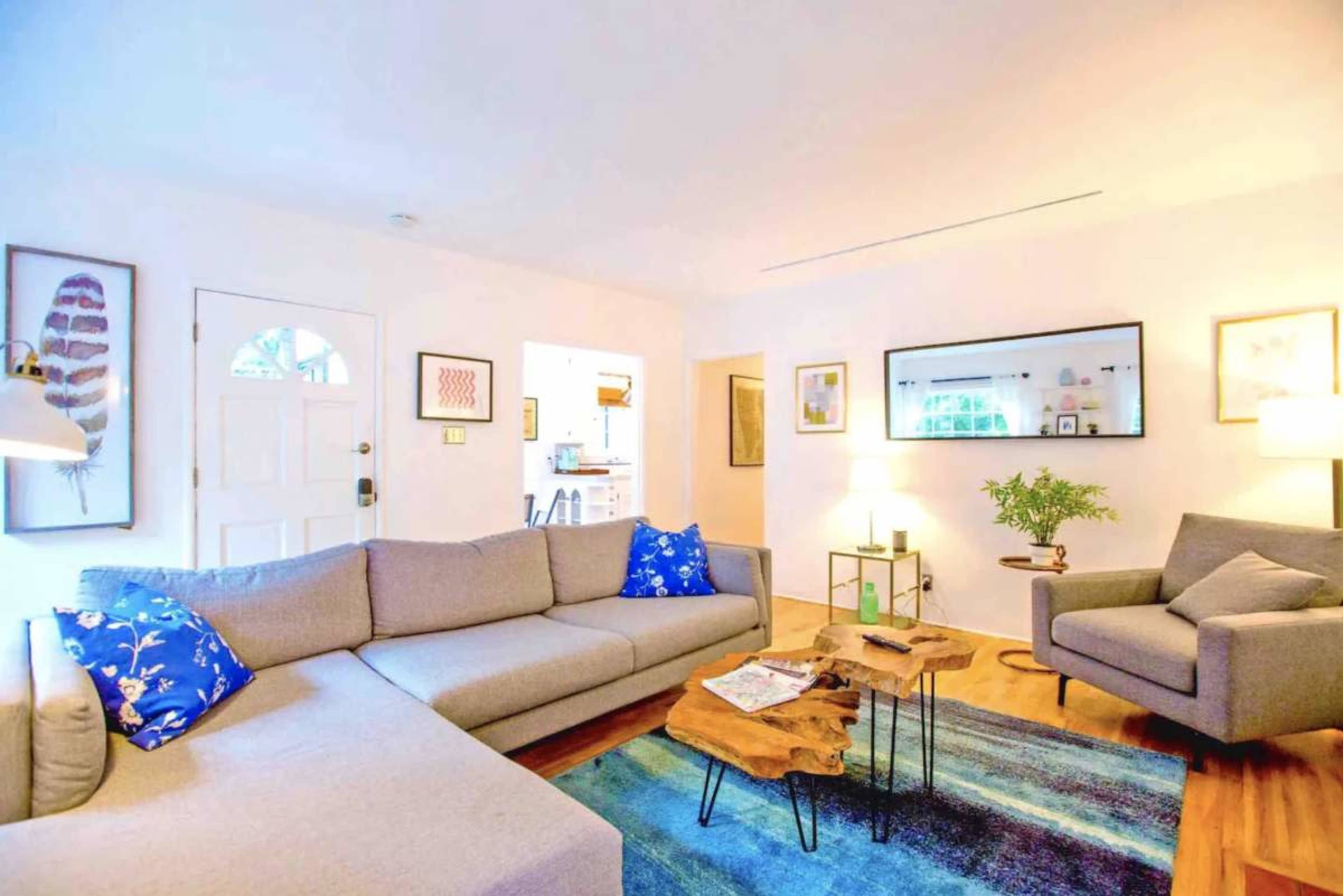 The living room features a gray sectional sofa, an armchair, a wooden coffee table, and colorful artwork on the walls.