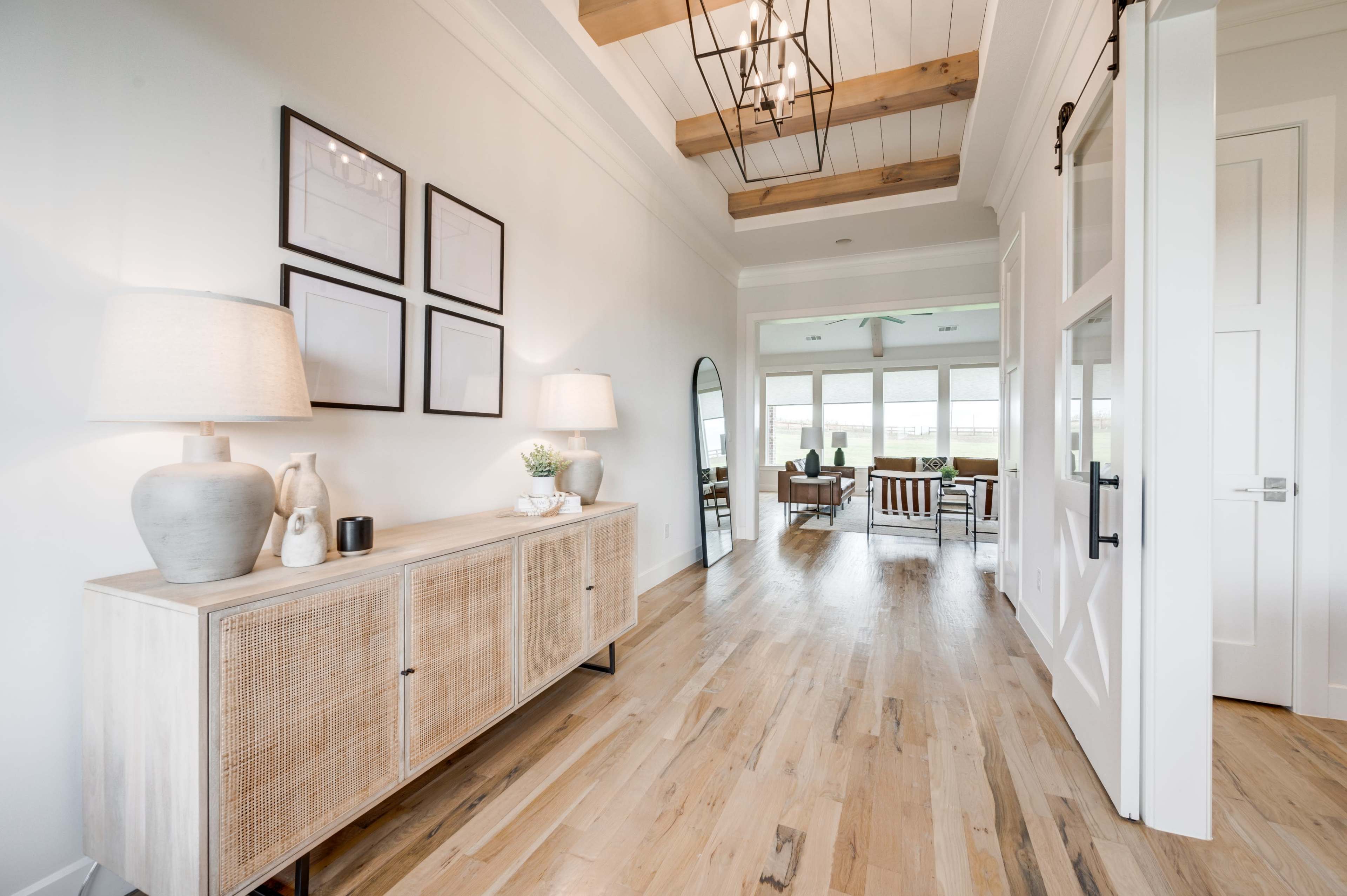 A foyer features a wooden console table with decorative items, framed art on the wall, and a large mirror, leading into a well-lit living space.