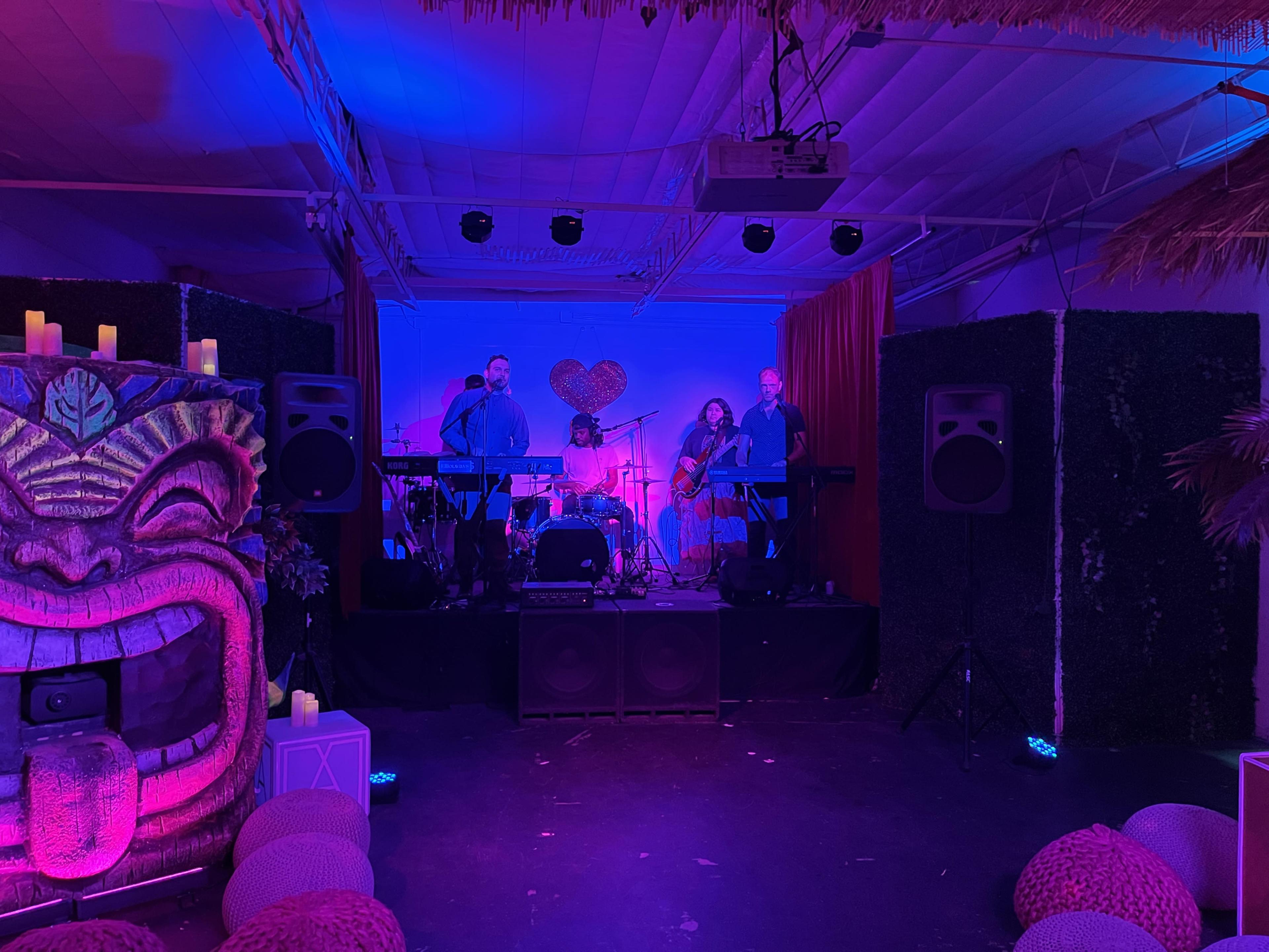 A band performs on a small stage decorated with tropical-themed artwork and ambient lighting.