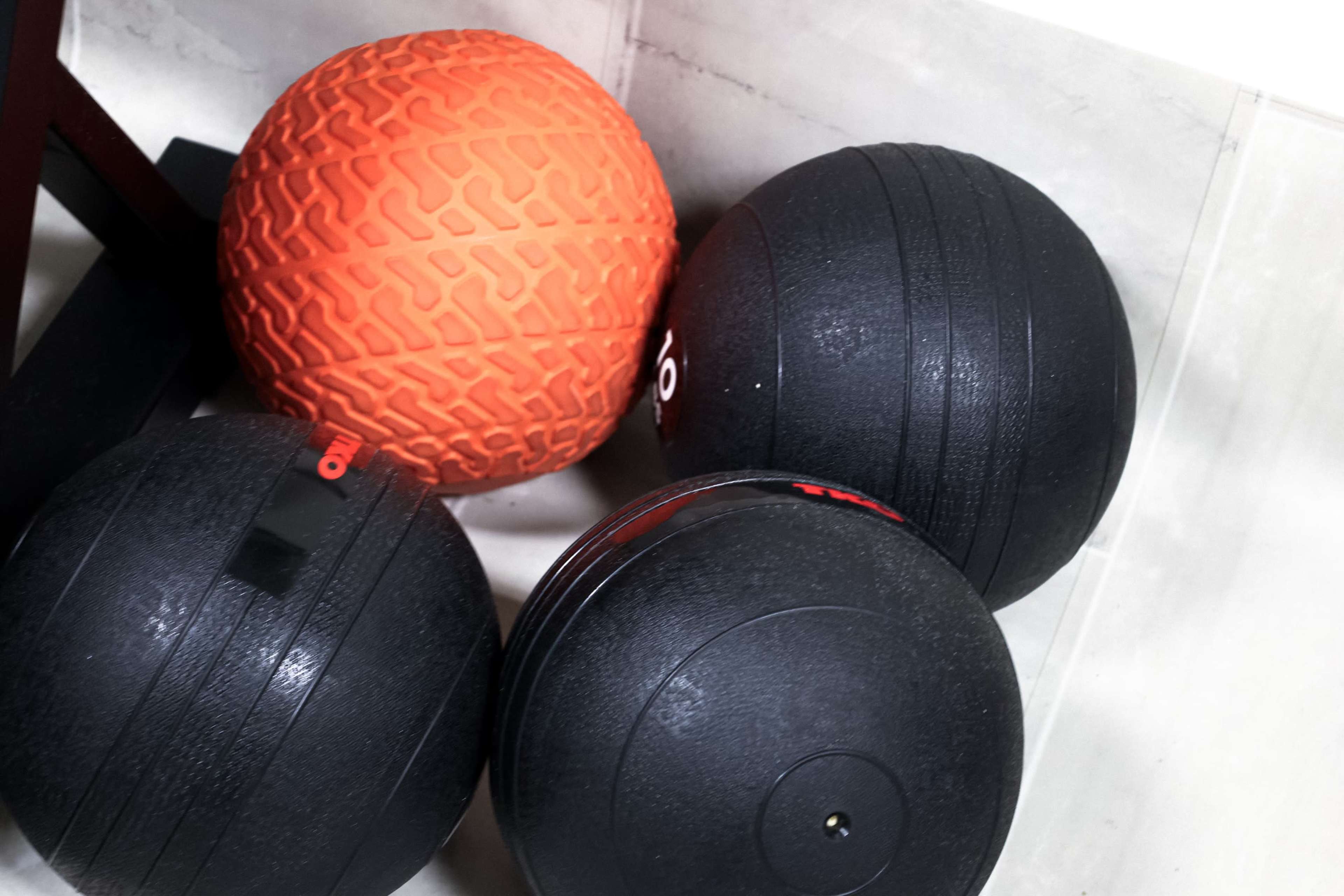 Four exercise balls, three black and one orange, resting on a tiled surface.