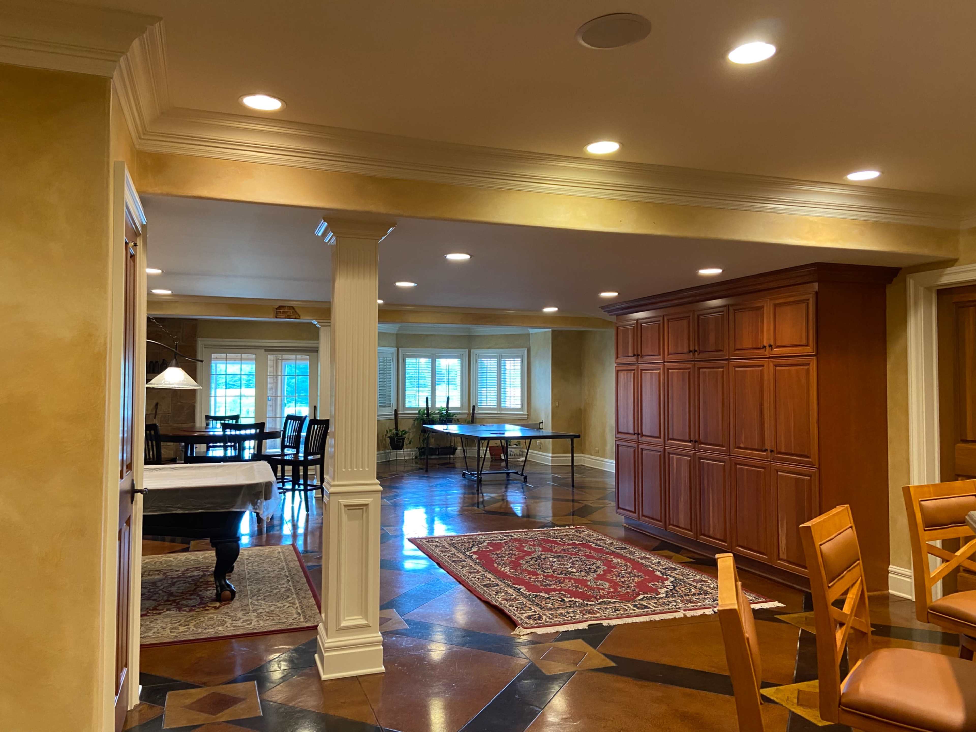 A spacious interior with a combination of wooden cabinetry, a dining area with chairs, and a game table in a well-lit room.