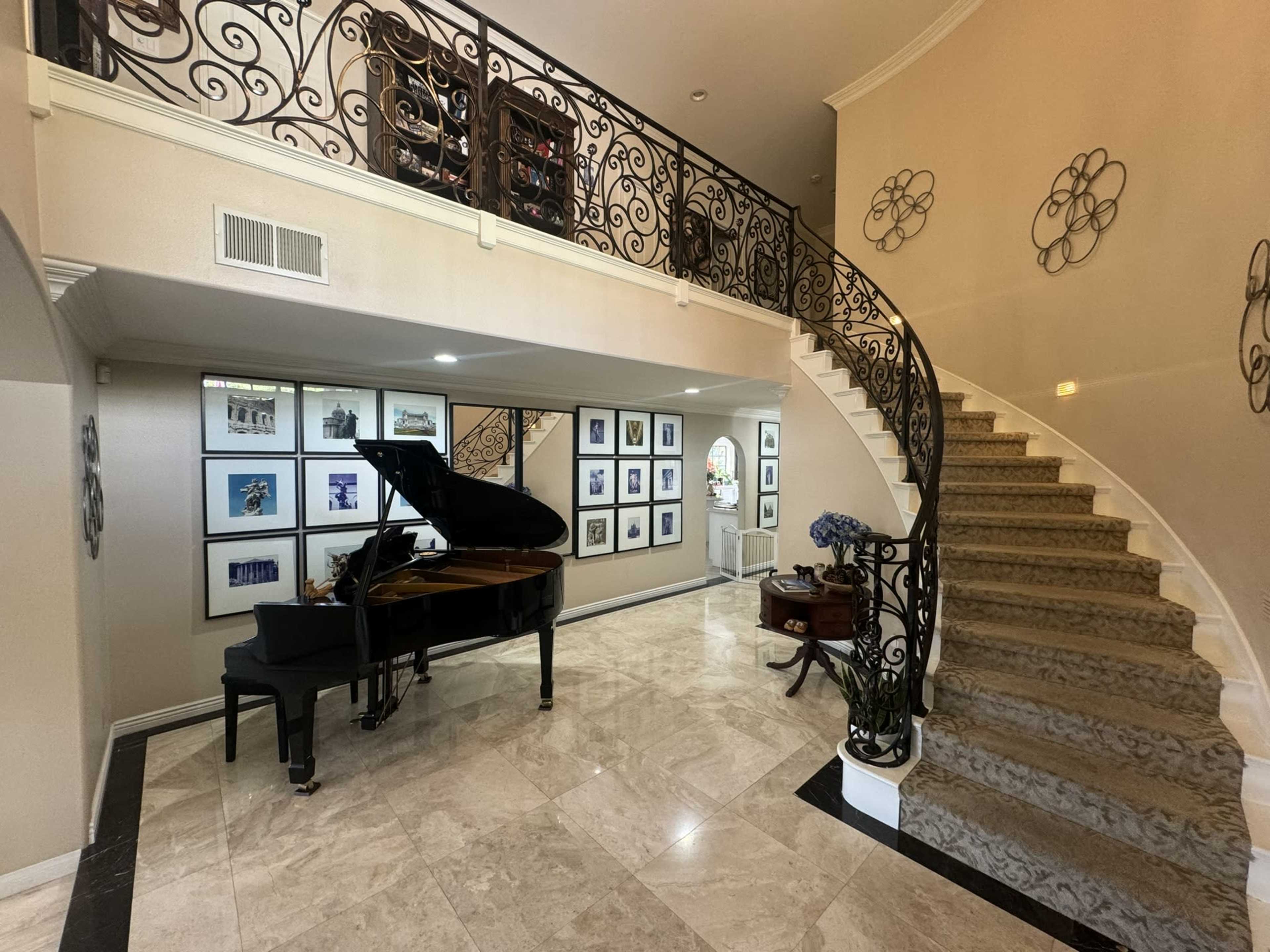 A spacious foyer with a grand staircase and a black piano located beside a wall adorned with framed photographs.