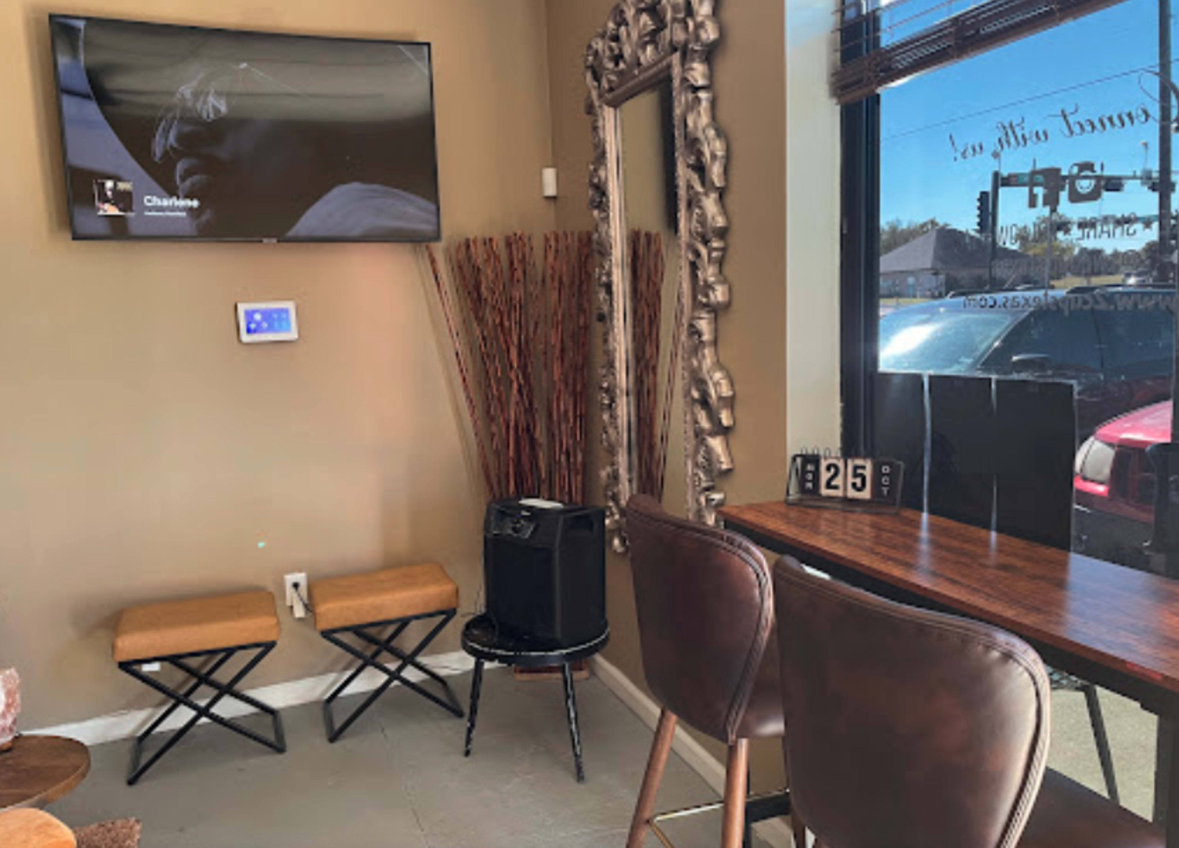 A cozy corner of a cafe featuring a television mounted on the wall, a decorative mirror, and a bar table with high stools.