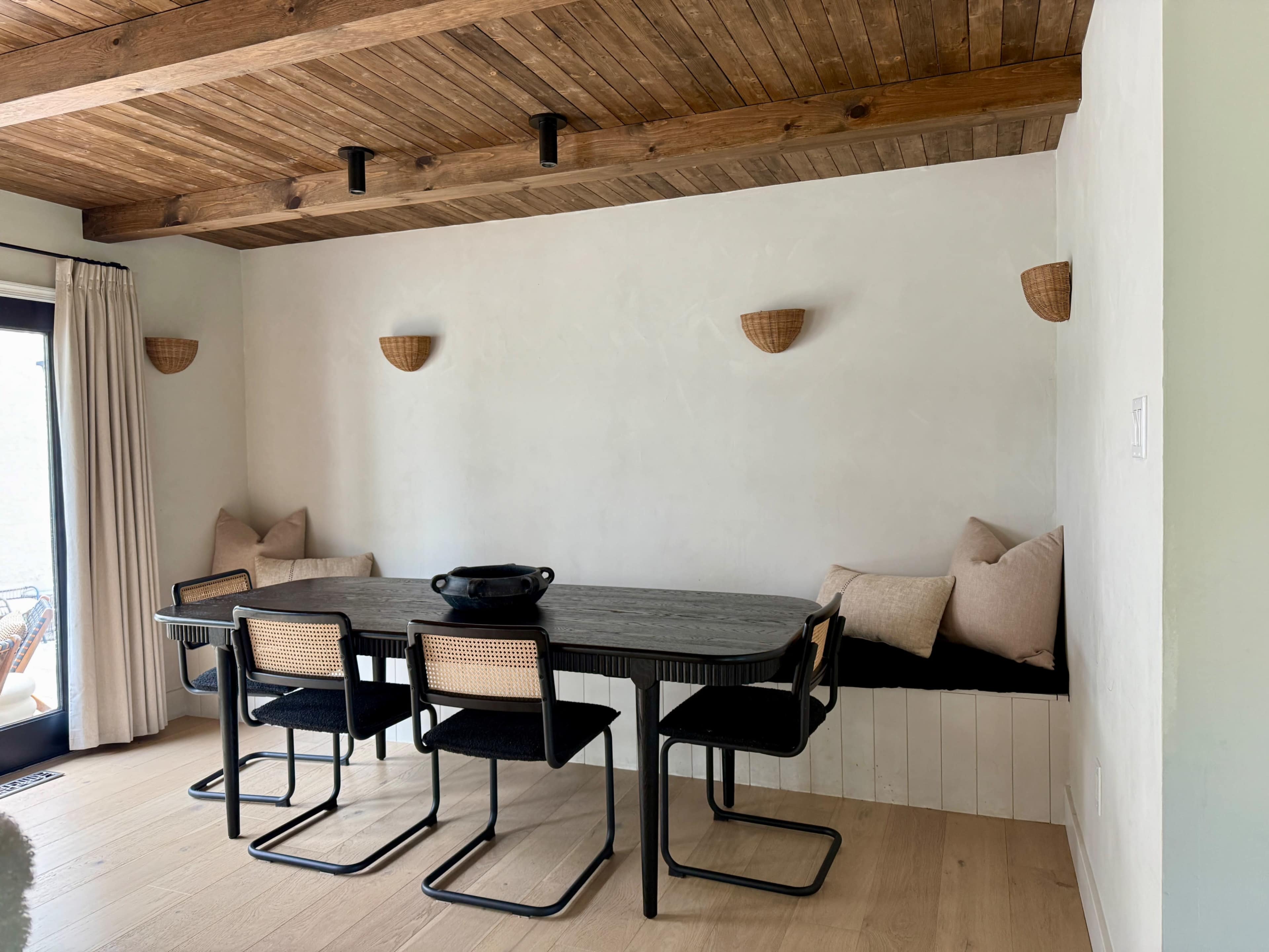A modern dining area features a large table surrounded by black chairs, with a built-in bench adorned with cushions along one wall.