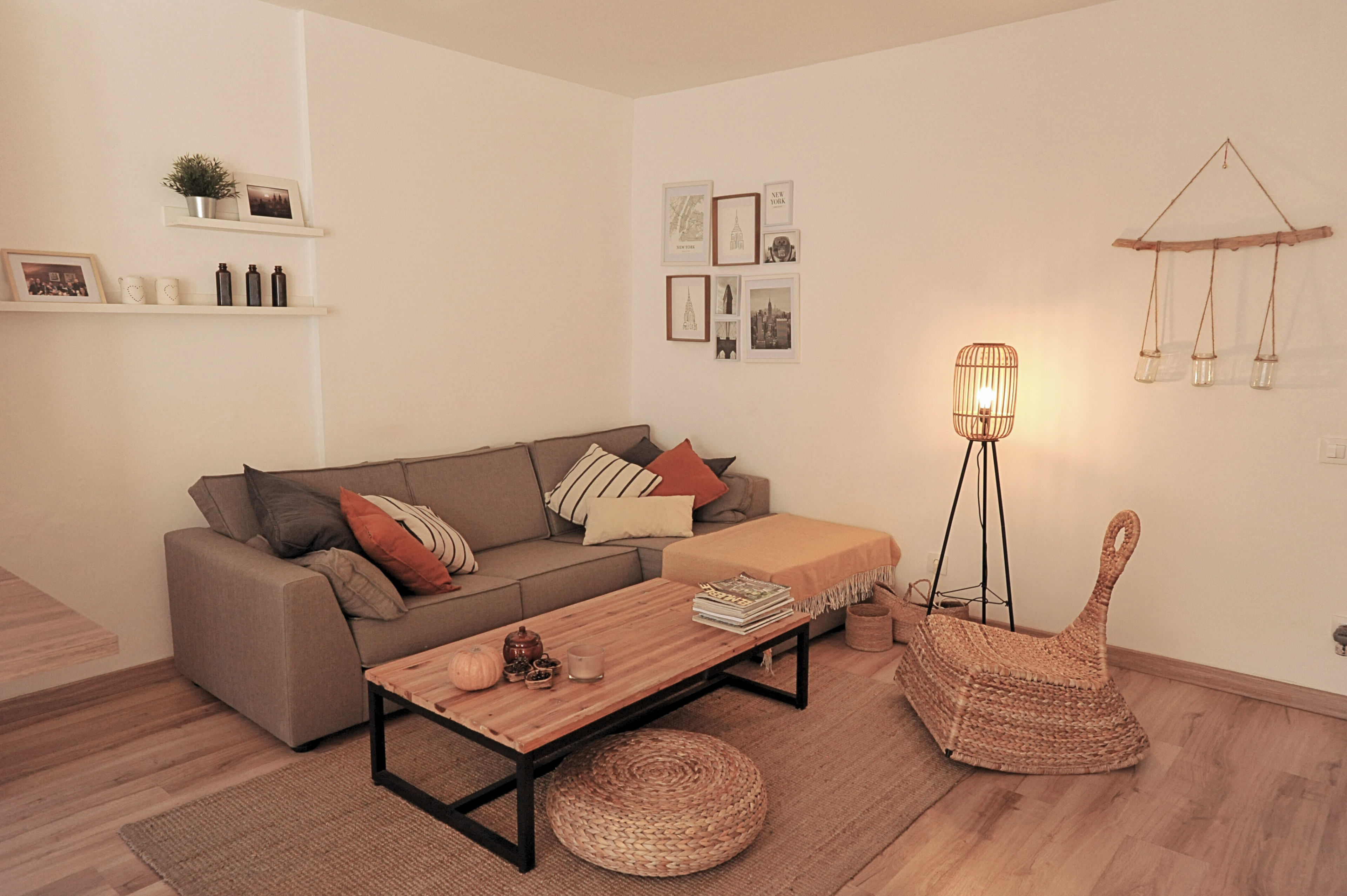The image shows a cozy living room featuring a gray sofa, a wooden coffee table, and a woven chair, with decorative items and artwork on the walls.