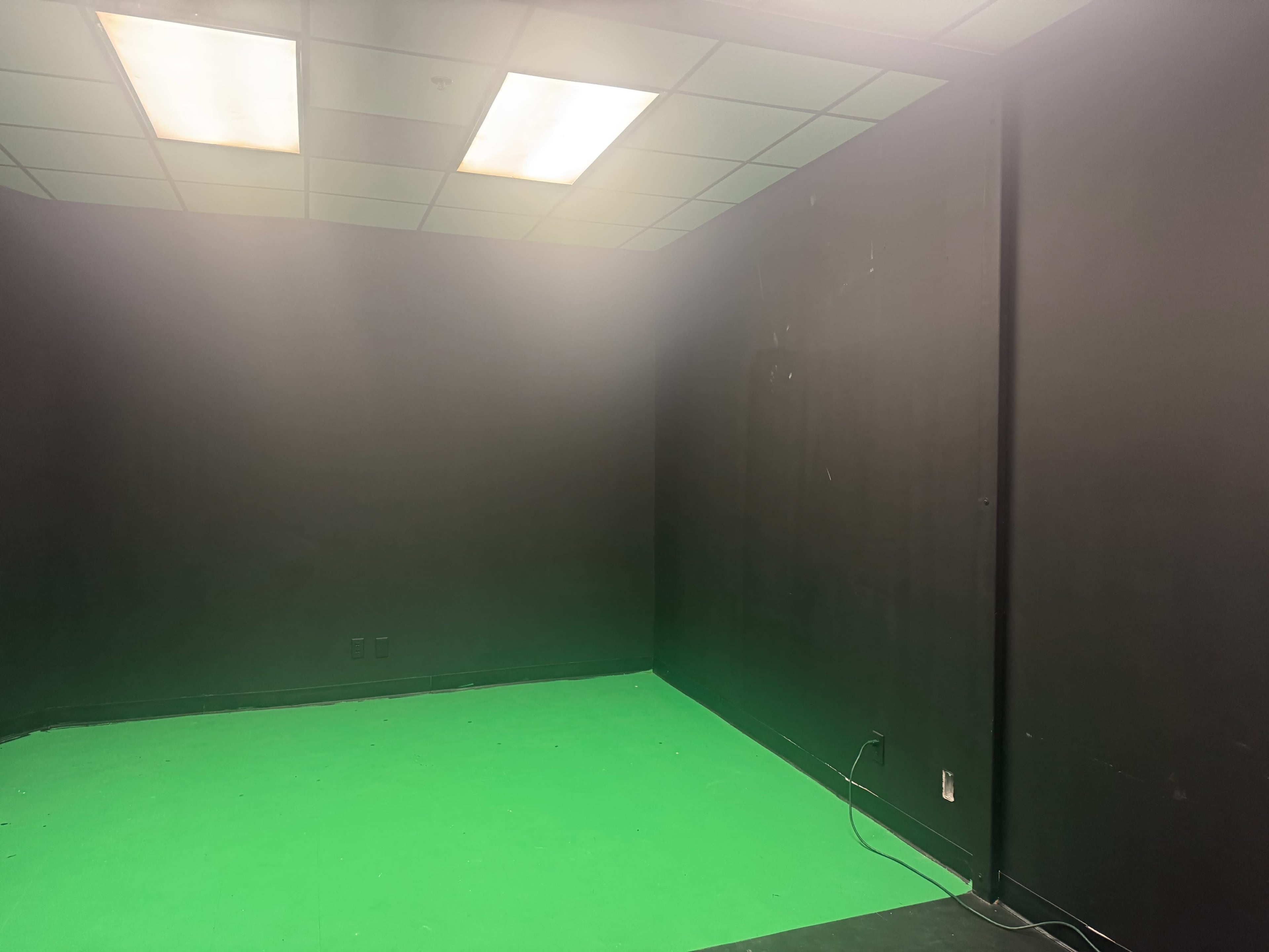 The image shows an empty room with black walls and a green floor, possibly a green screen studio.