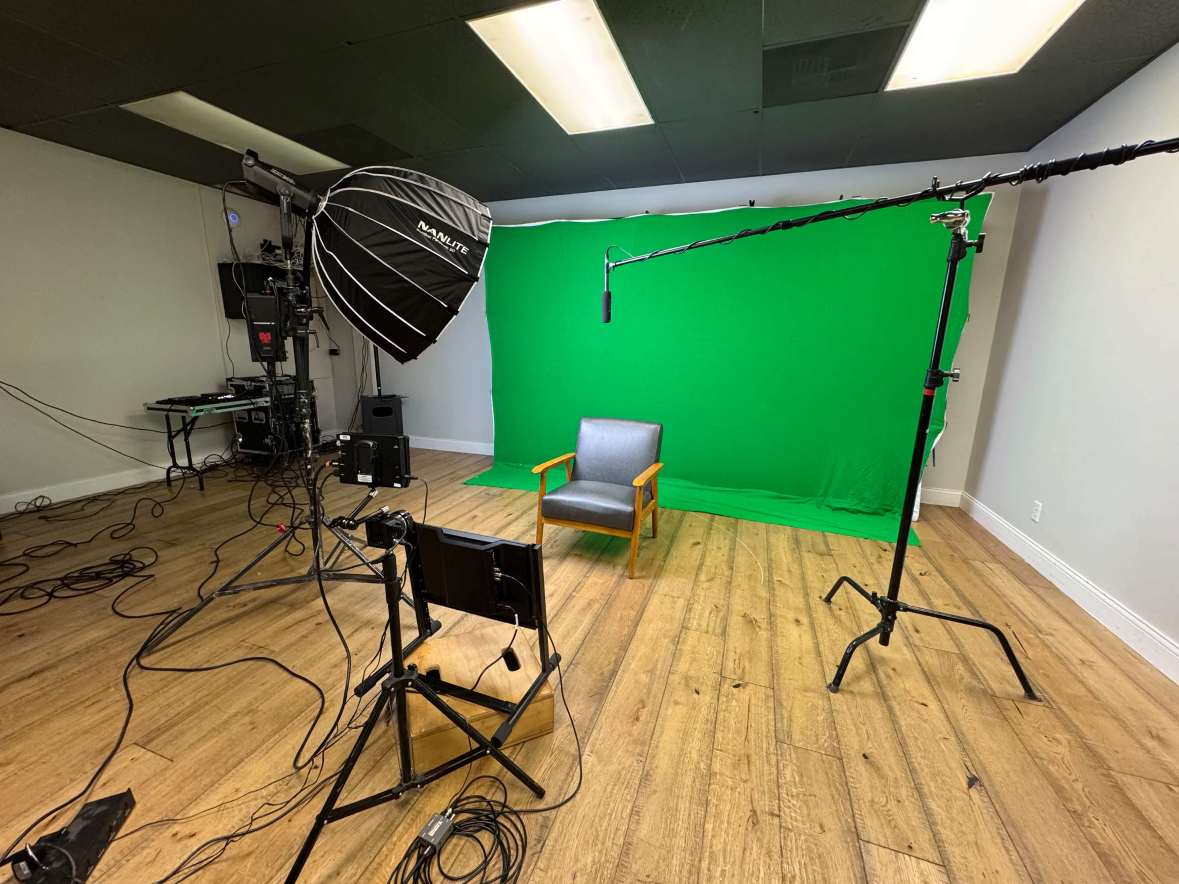 The image shows a video production setup with a green screen, a chair in the center, and various lighting and microphone equipment arranged around the scene.