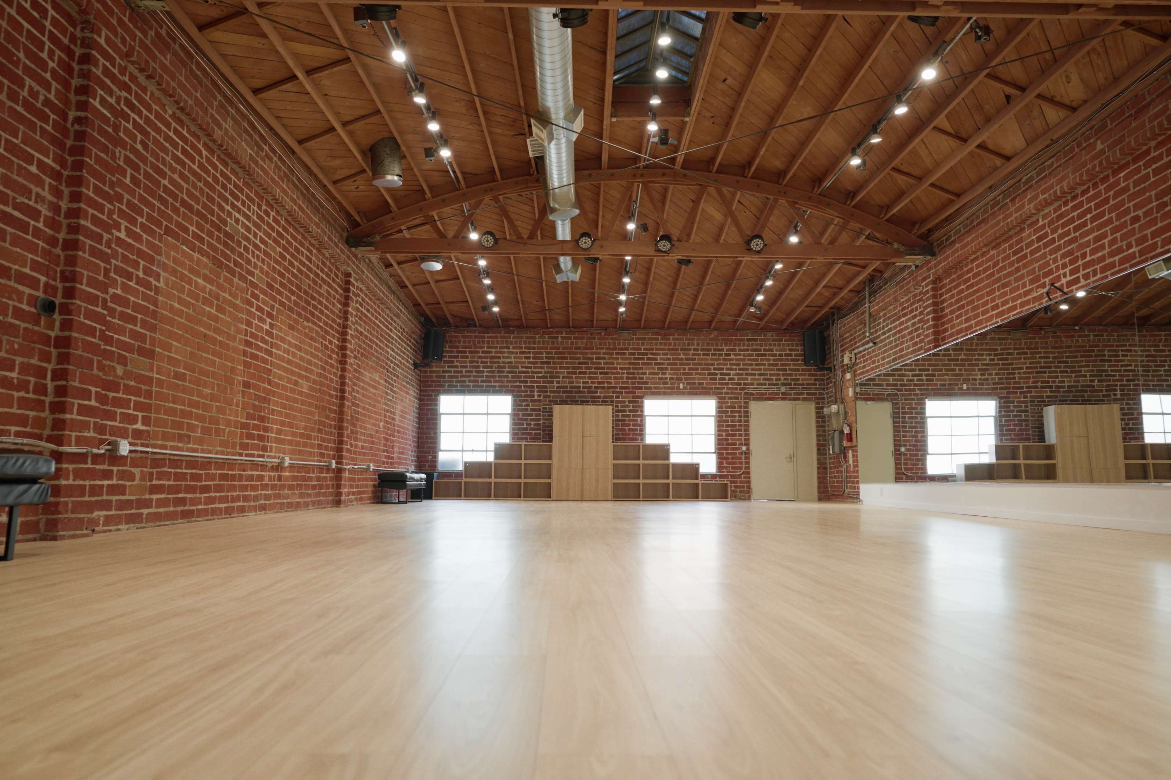A spacious studio with wooden floors, exposed brick walls, and large windows.