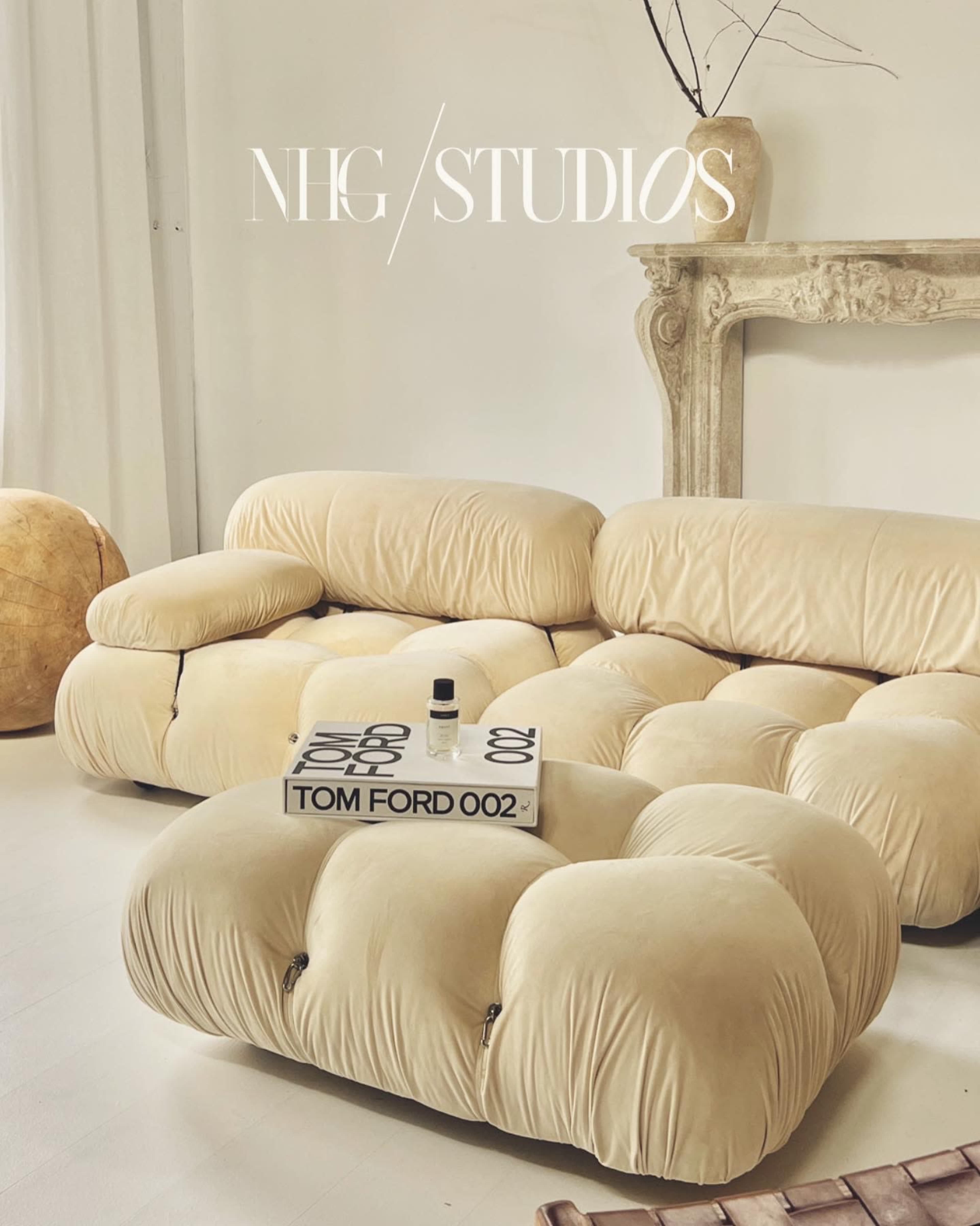 A beige, plush sectional sofa in a well-lit room with a small decorative table displaying a Tom Ford book and a bottle.