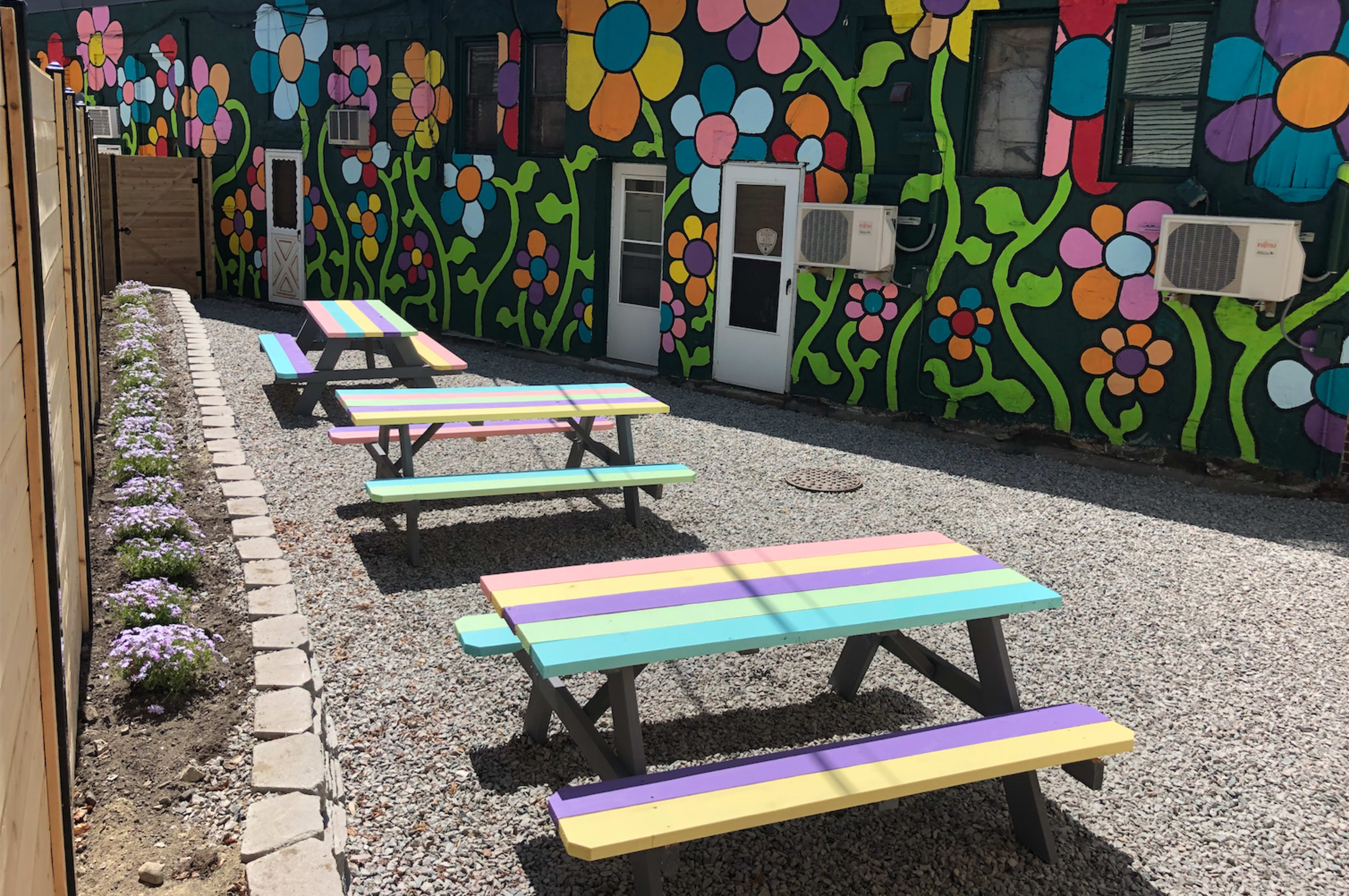 A colorful outdoor area with picnic tables and a vibrant floral mural on the wall.