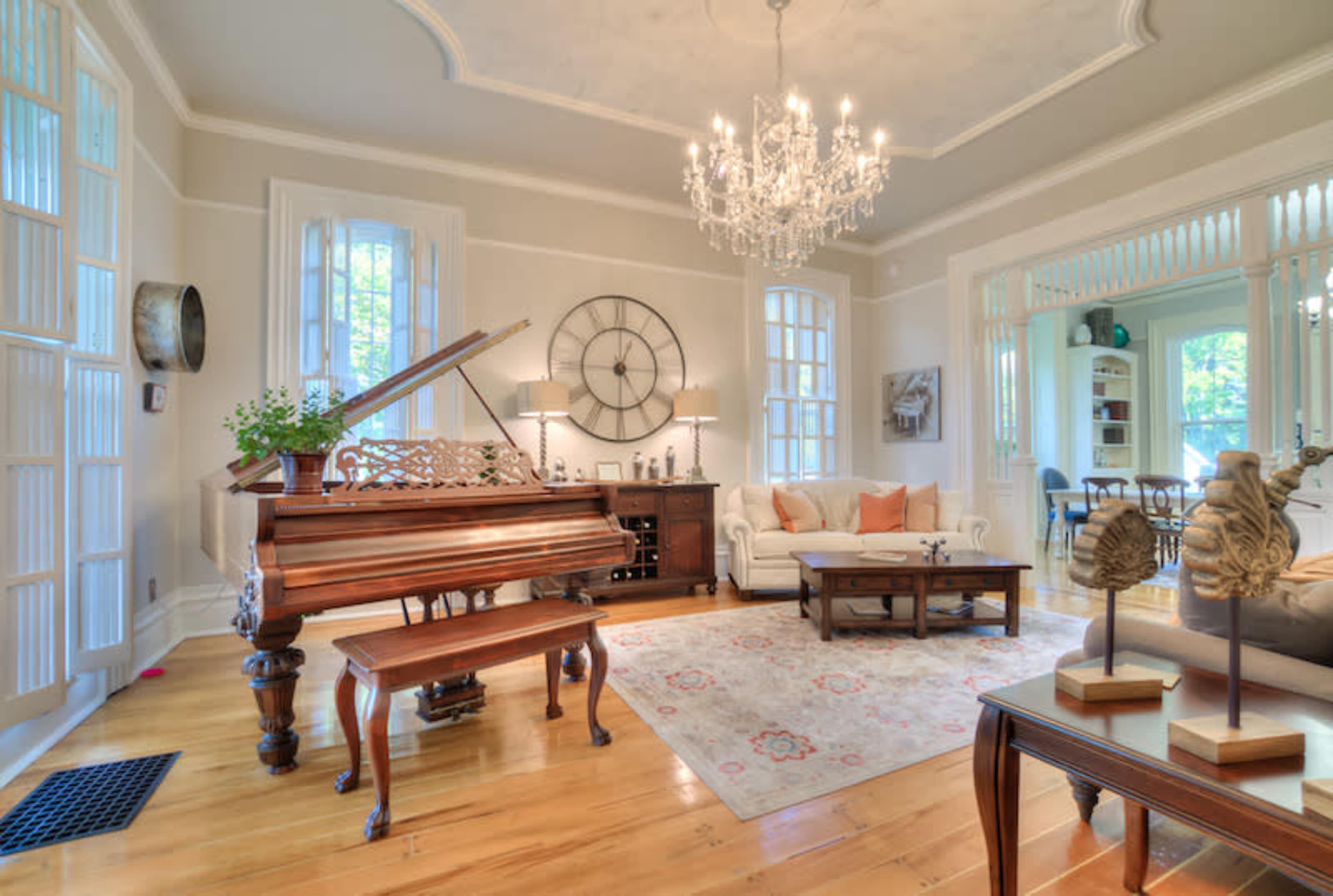 A well-lit living room with a grand piano, an elegant chandelier, and a sofa accompanied by a coffee table and decorative accents.