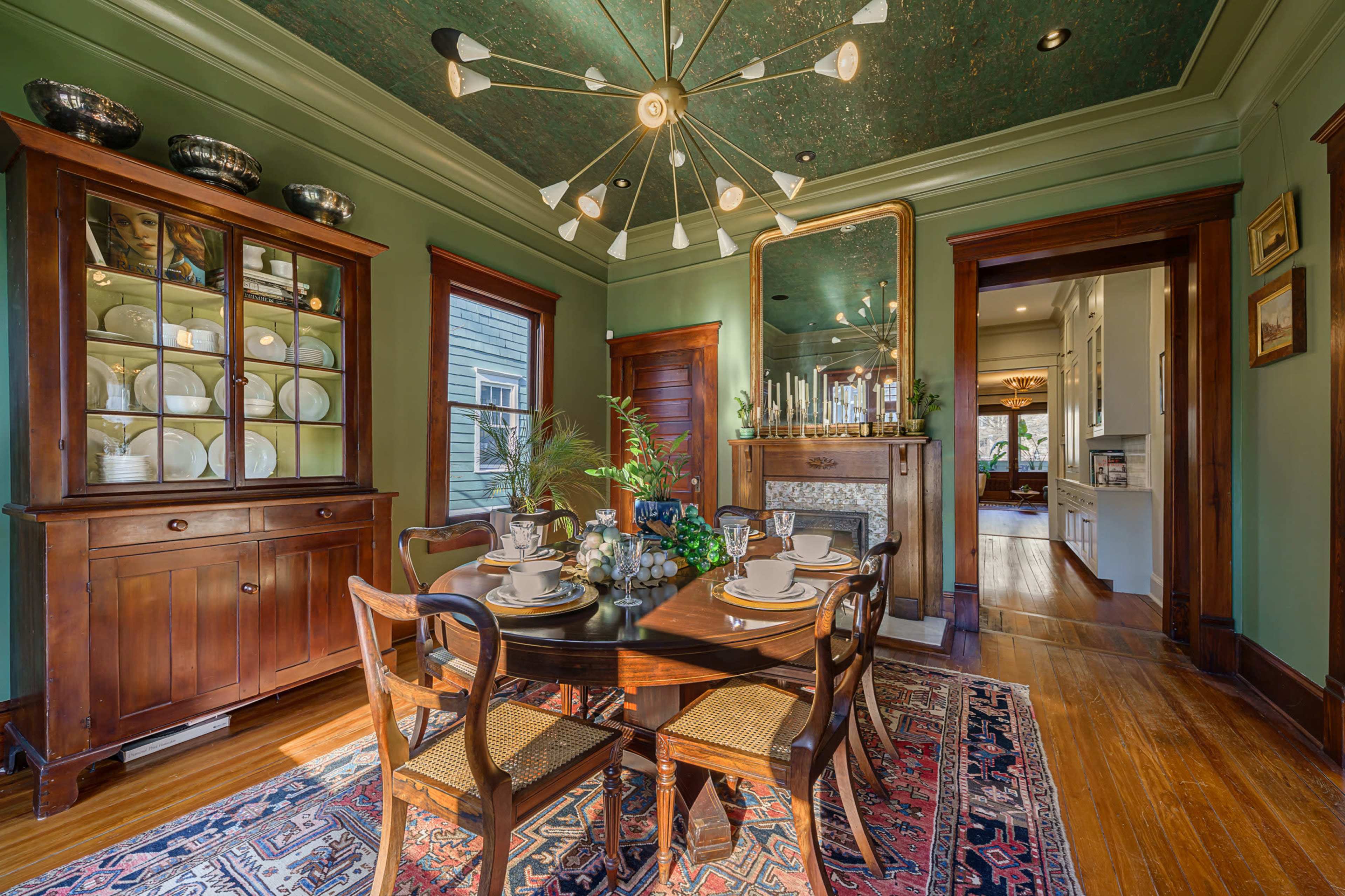 A dining room featuring a round table set for a meal, surrounded by four chairs, with a wooden hutch displaying dishware and a mirror on the wall reflecting the space.