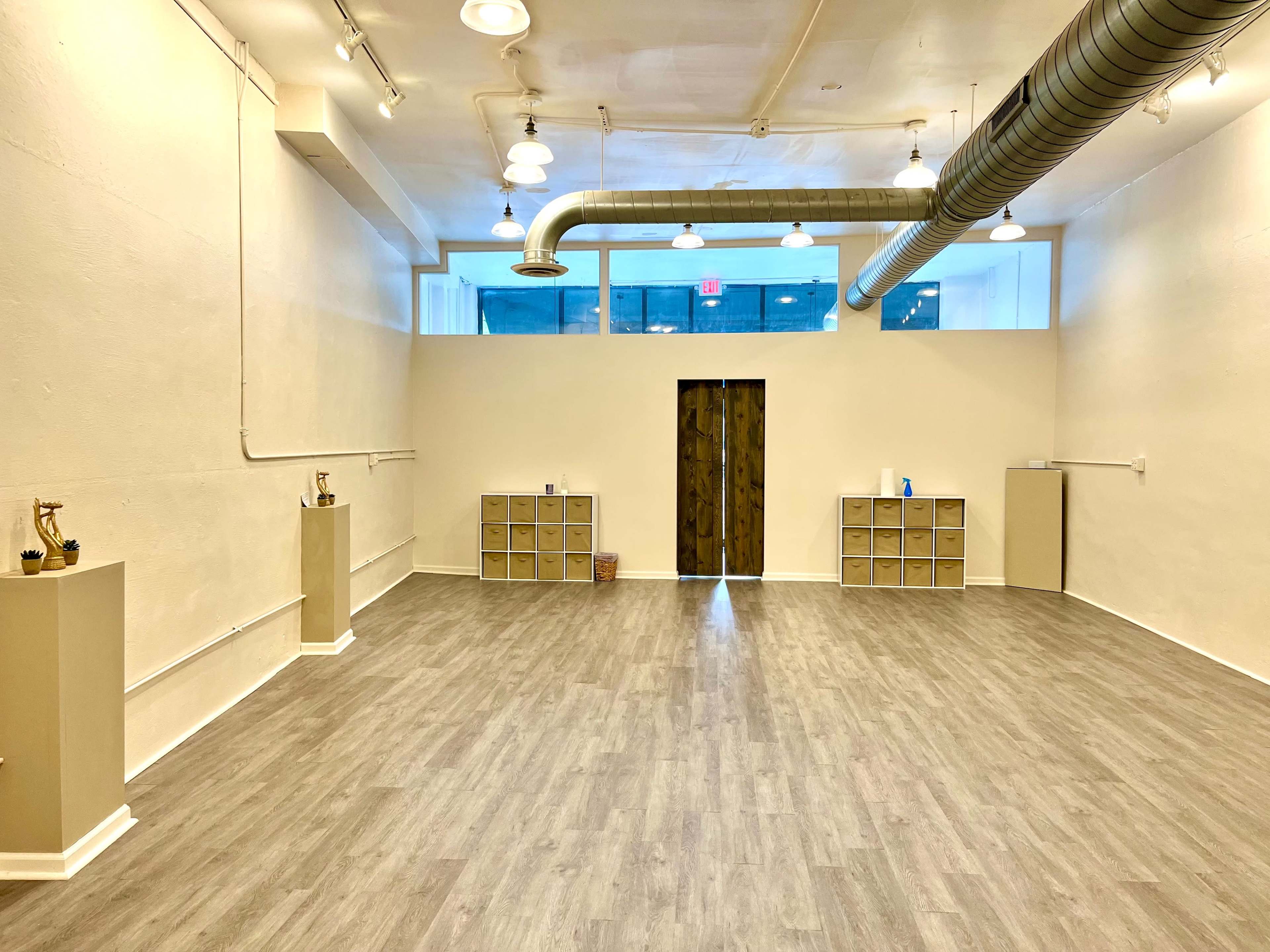 A spacious, brightly lit interior room with wooden flooring, featuring two cabinets on opposite walls, and a wooden door at the far end.