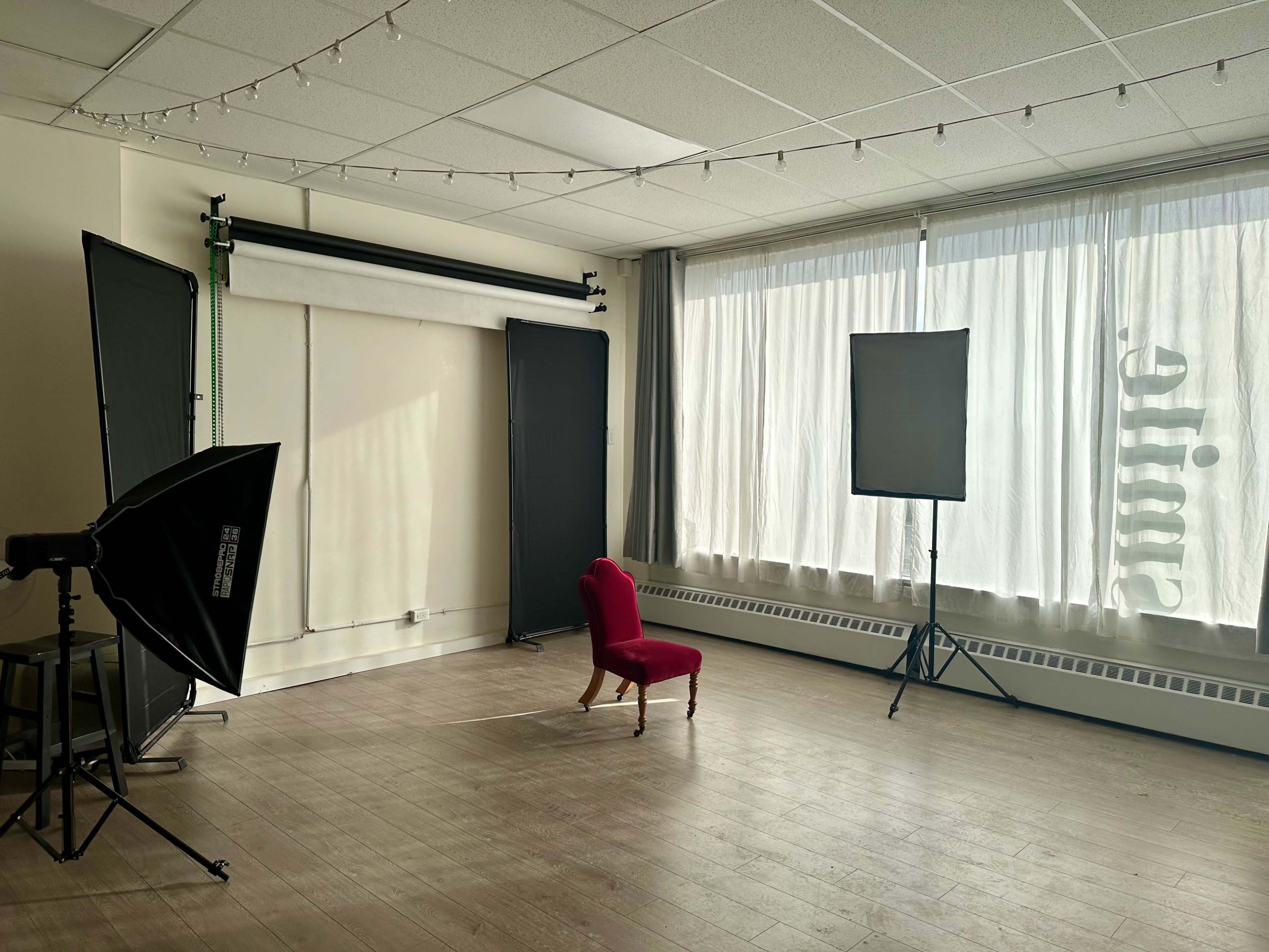 A brightly lit photo studio featuring a solitary red chair in the center, surrounded by softbox lighting equipment and a backdrop.