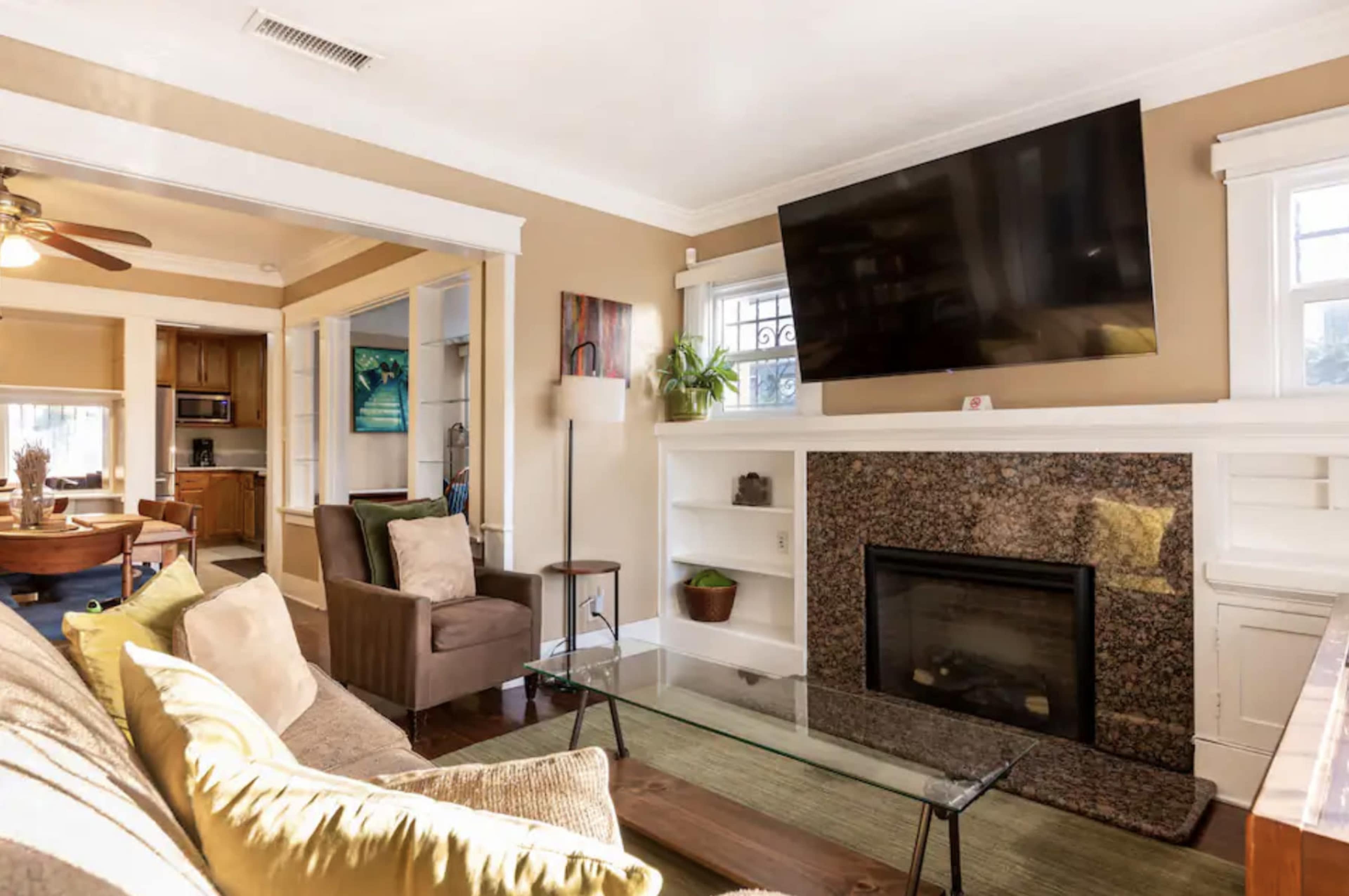 The image shows a living room with a sofa, armchair, flat-screen television mounted on the wall, and a stone fireplace beneath it.