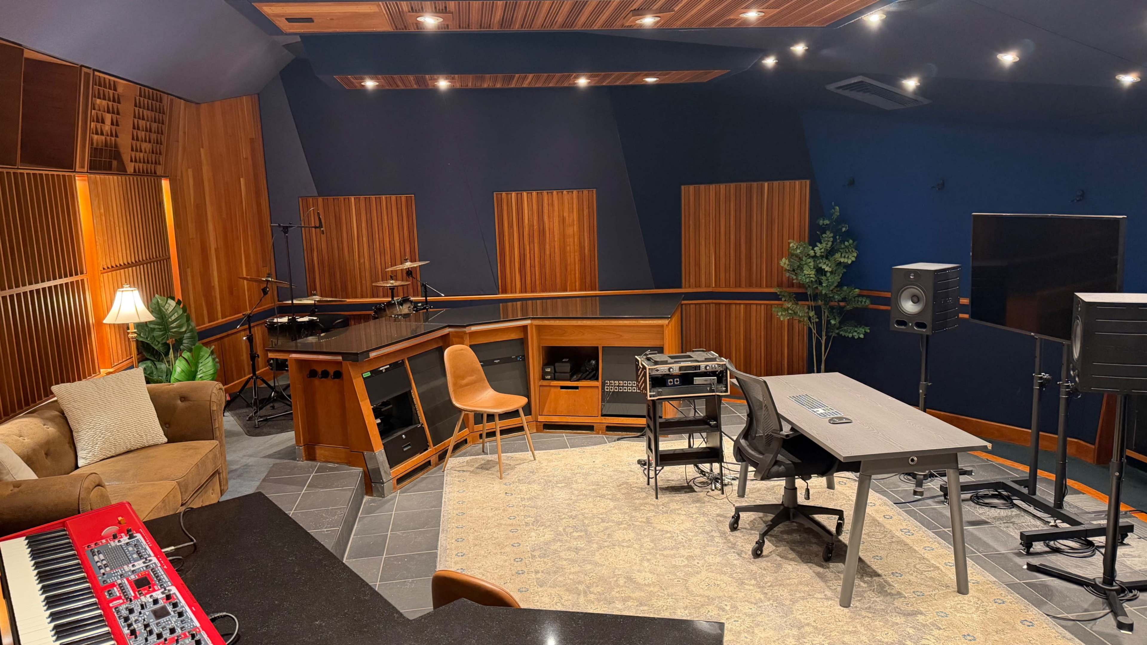 The image depicts a music studio with wooden paneling, a desk with equipment, a chair, and various musical instruments in the background.