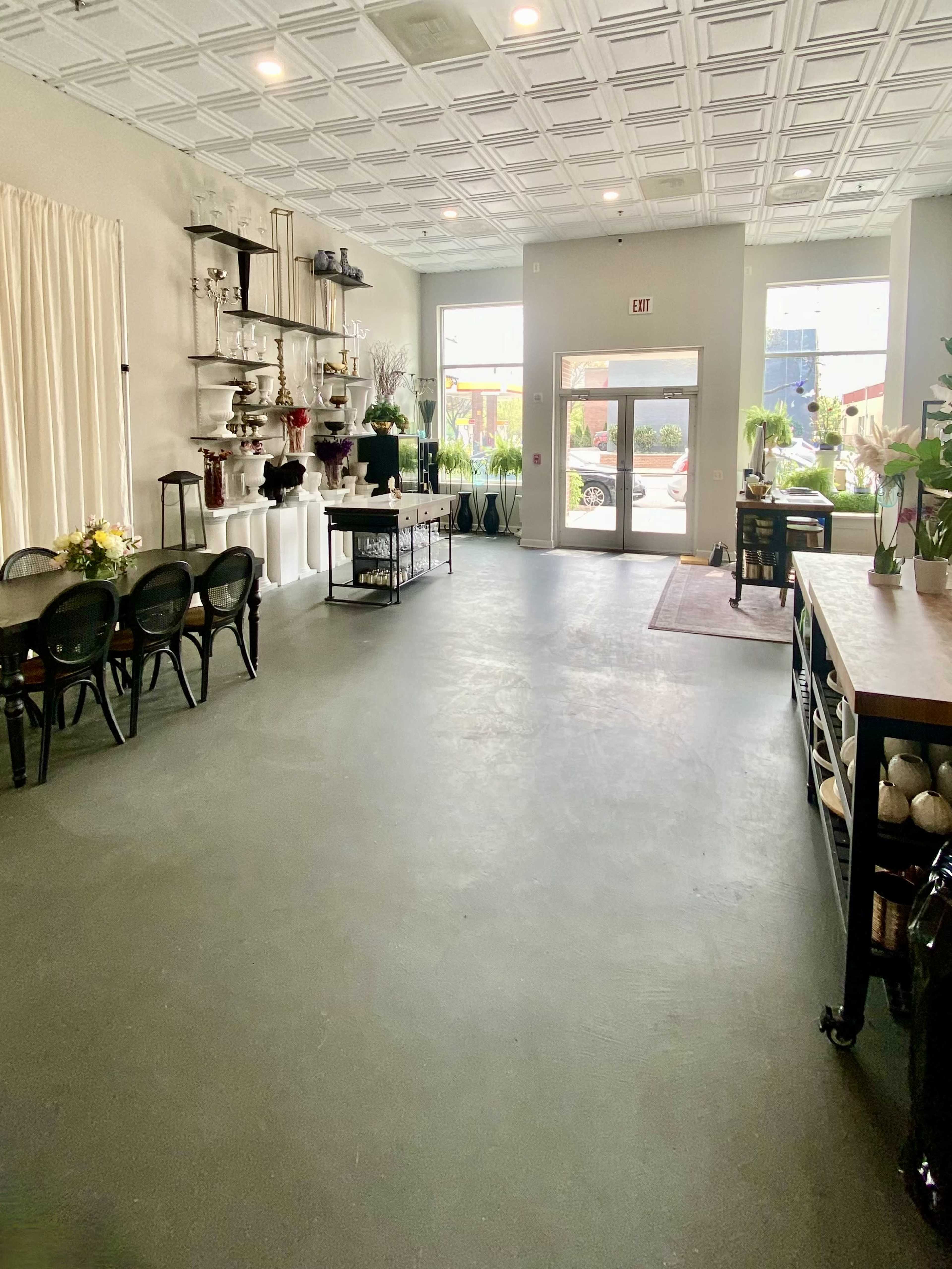 A well-organized floral shop interior featuring a seating area, shelves with decorative items, and large windows providing natural light.