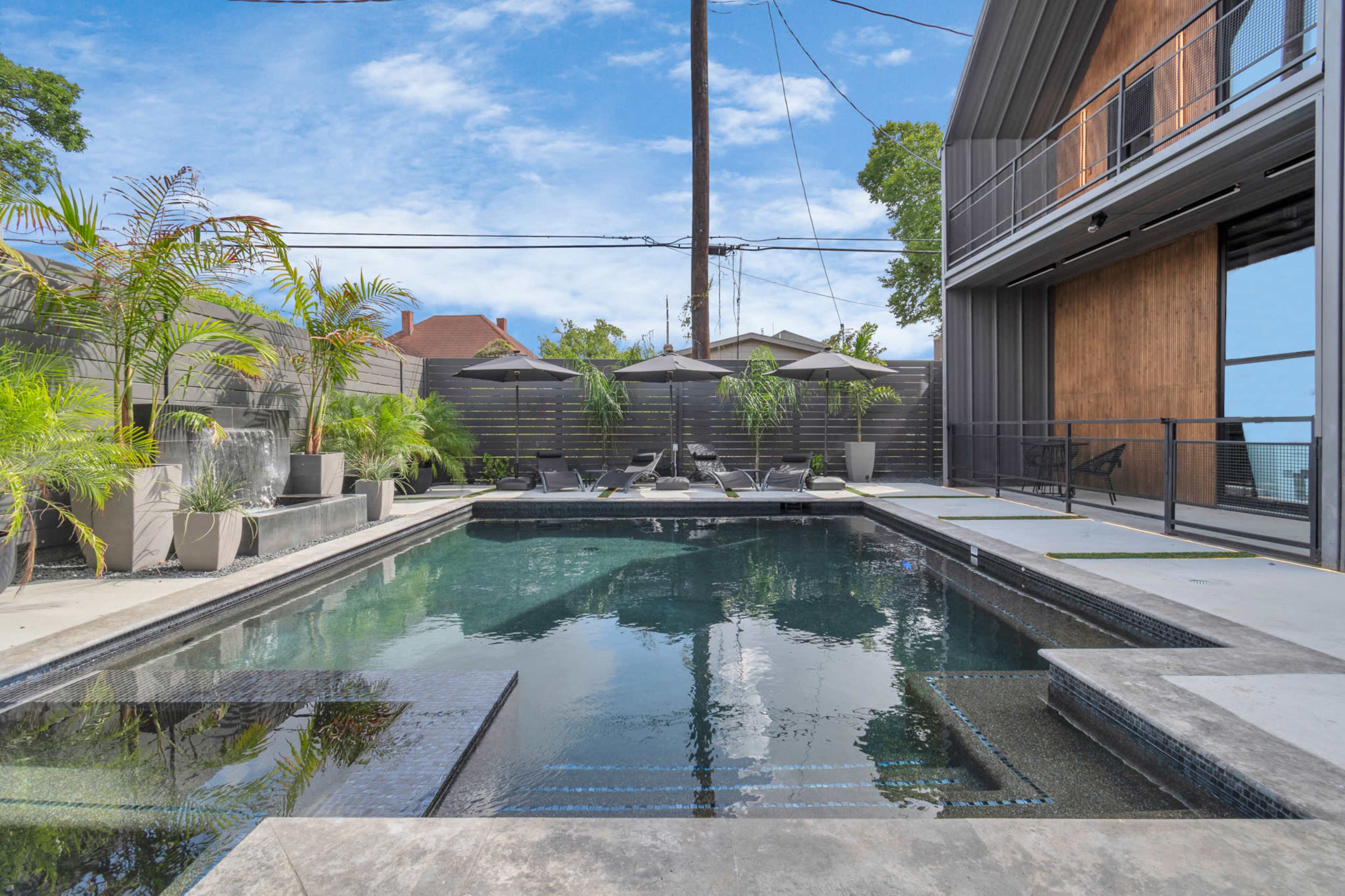 A modern outdoor space featuring a rectangular swimming pool surrounded by lounge chairs and large planters with plants.