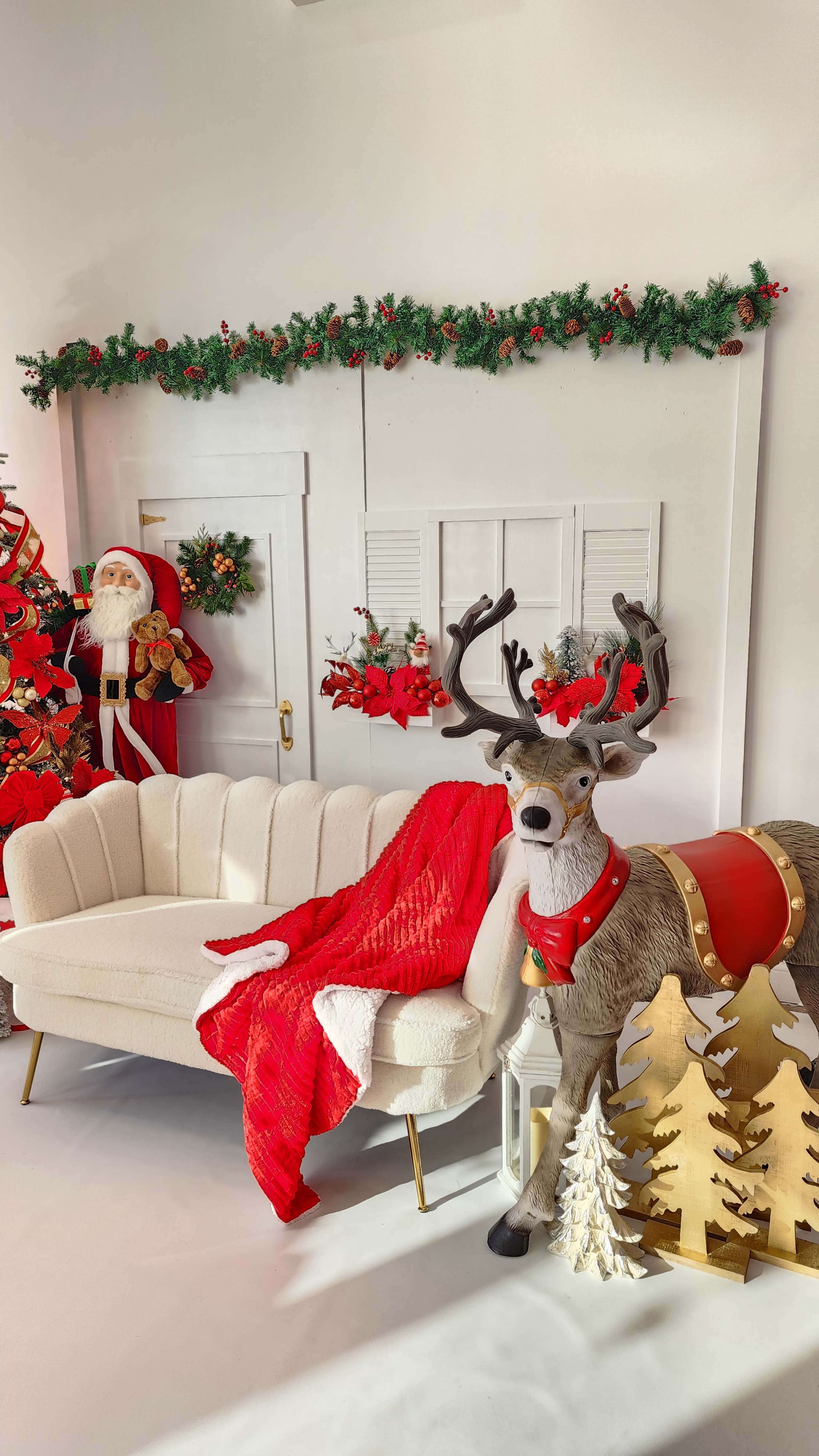 The scene features a festive living room decorated for Christmas, showcasing a cozy white couch, a large reindeer figure, and a Santa Claus figure against a backdrop of garlands and holiday decor.