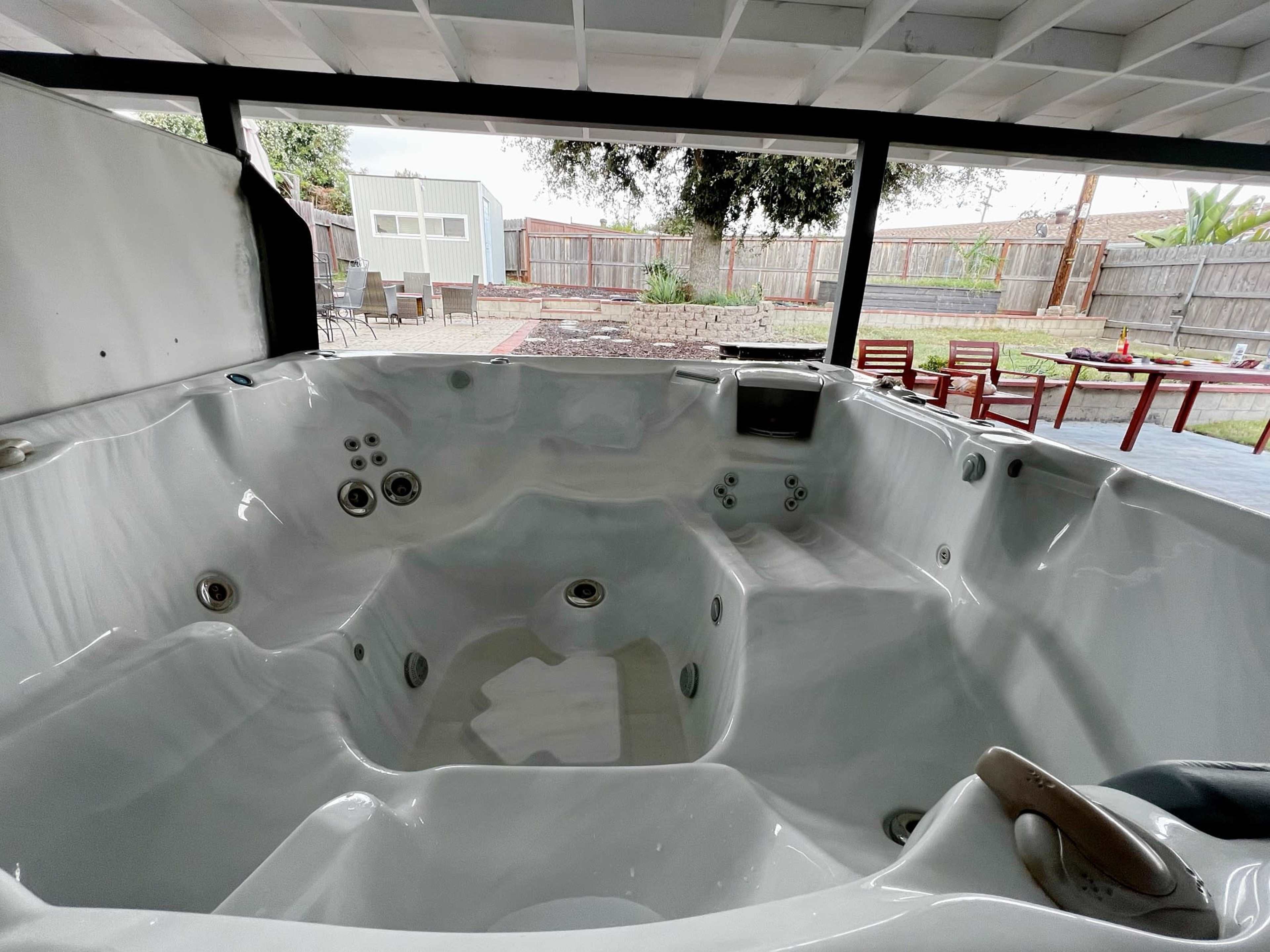 A spacious, empty hot tub set within a covered outdoor area, overlooking a backyard with seating and a shed in the distance.