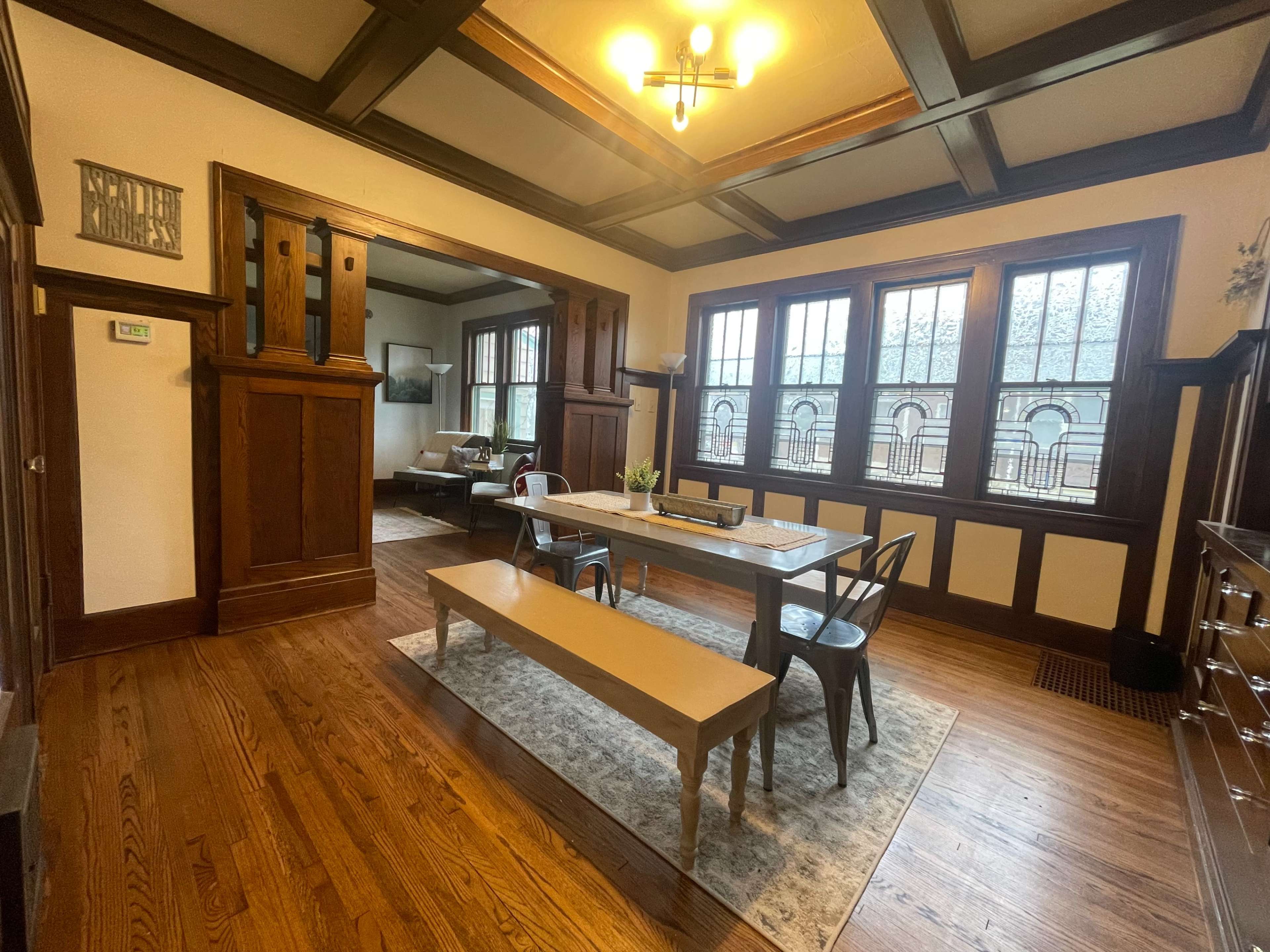 A spacious dining area features a long table with metal chairs, surrounded by large windows and wooden architectural details.