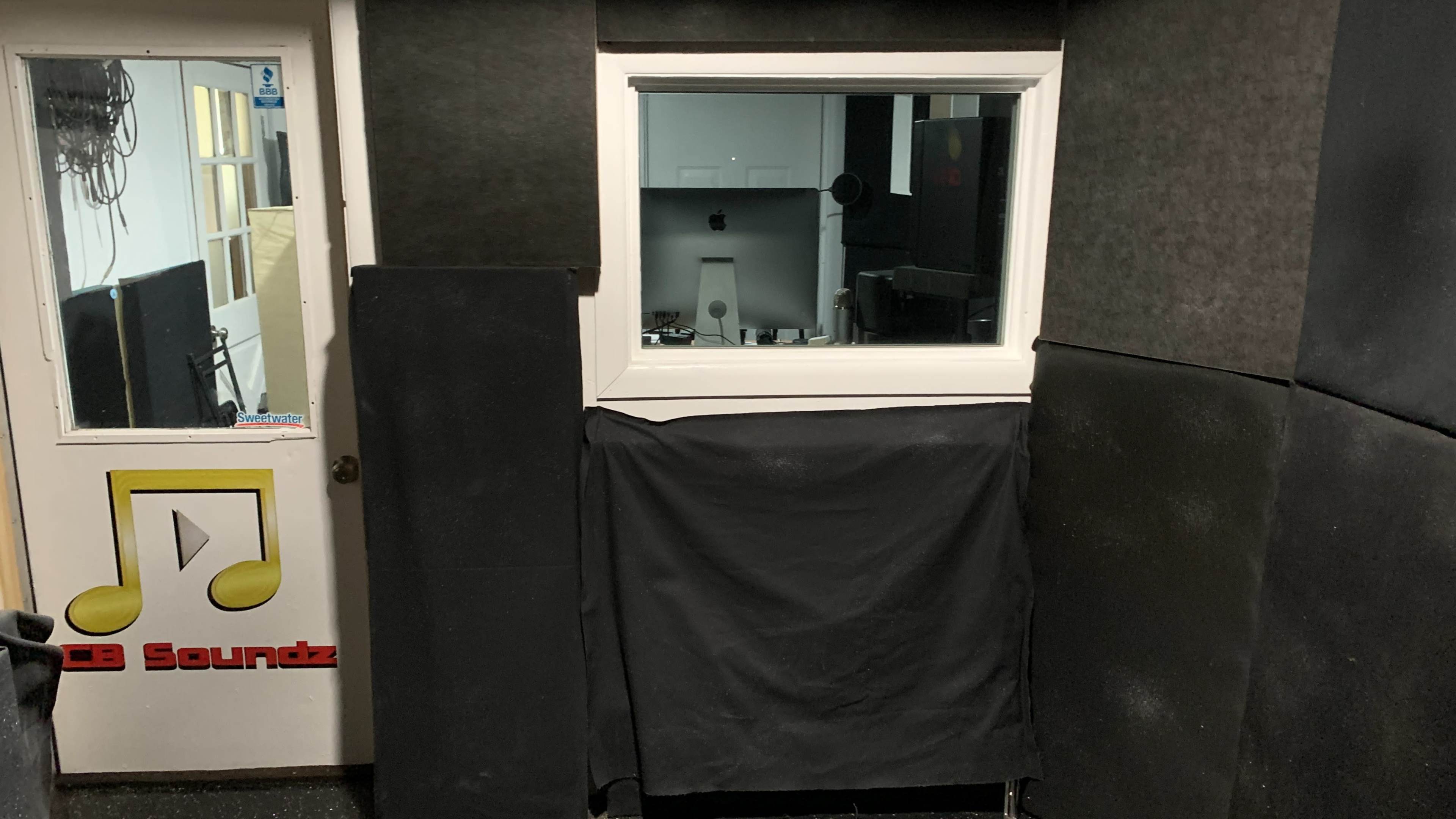 The image shows a soundproof recording studio with a window overlooking a control area equipped with a computer and sound equipment.