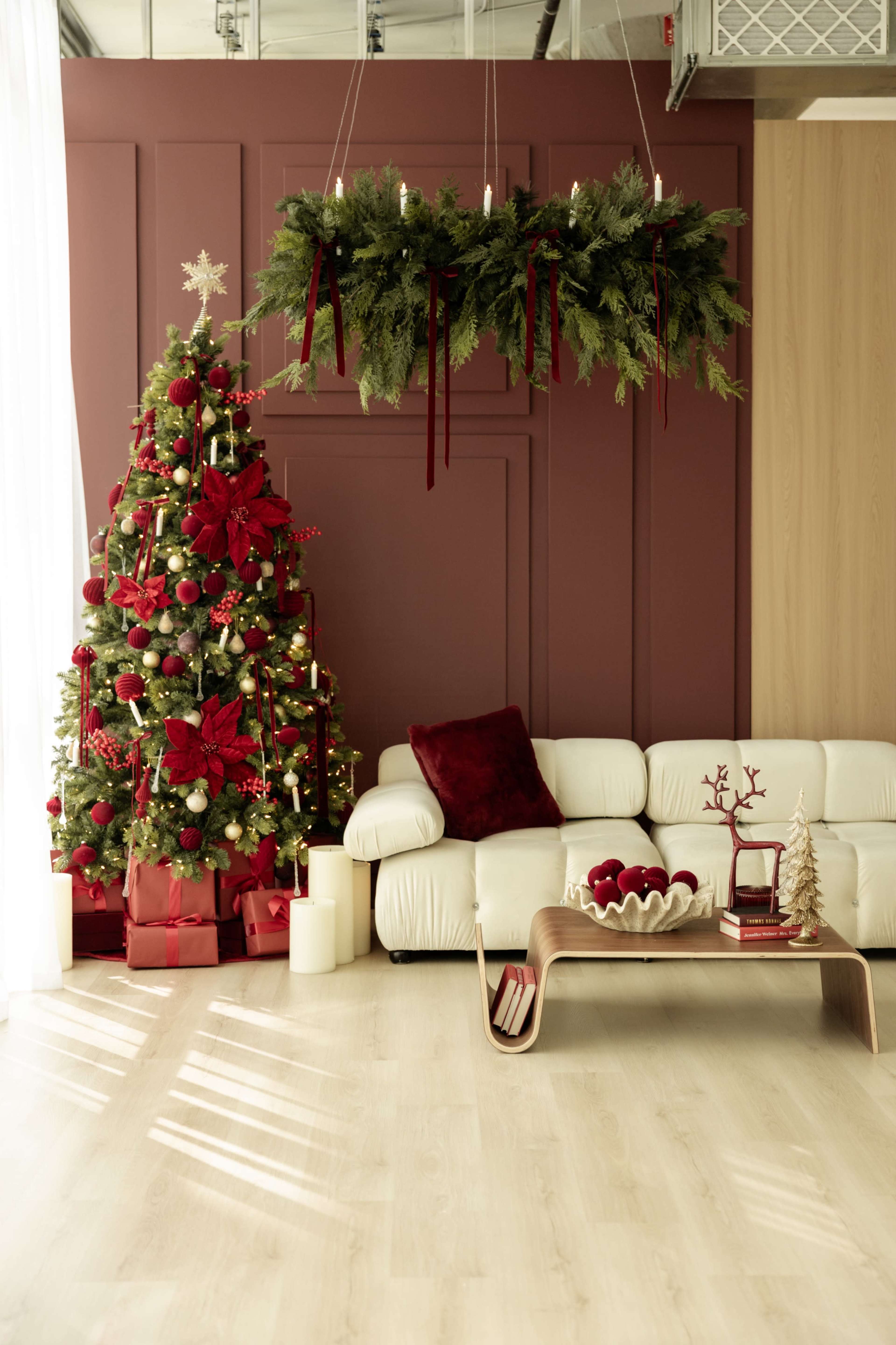 A Christmas-themed living room features a decorated tree, a white couch, and festive decorations on a wooden table.