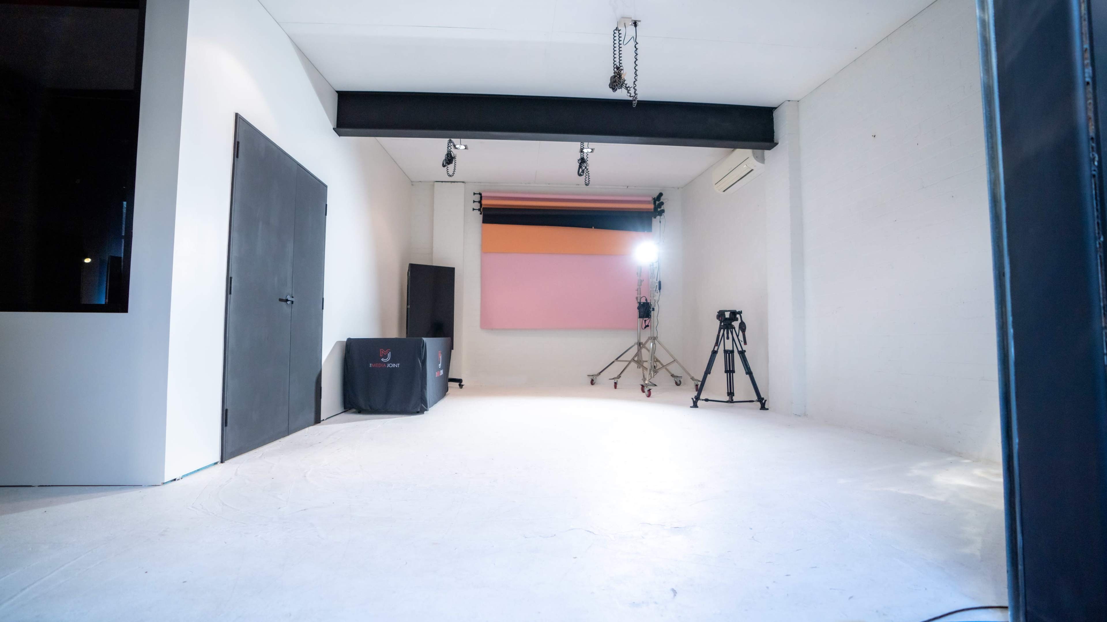 A spacious studio with white walls, a softbox lighting setup, a blank backdrop, and a tripod for photography.