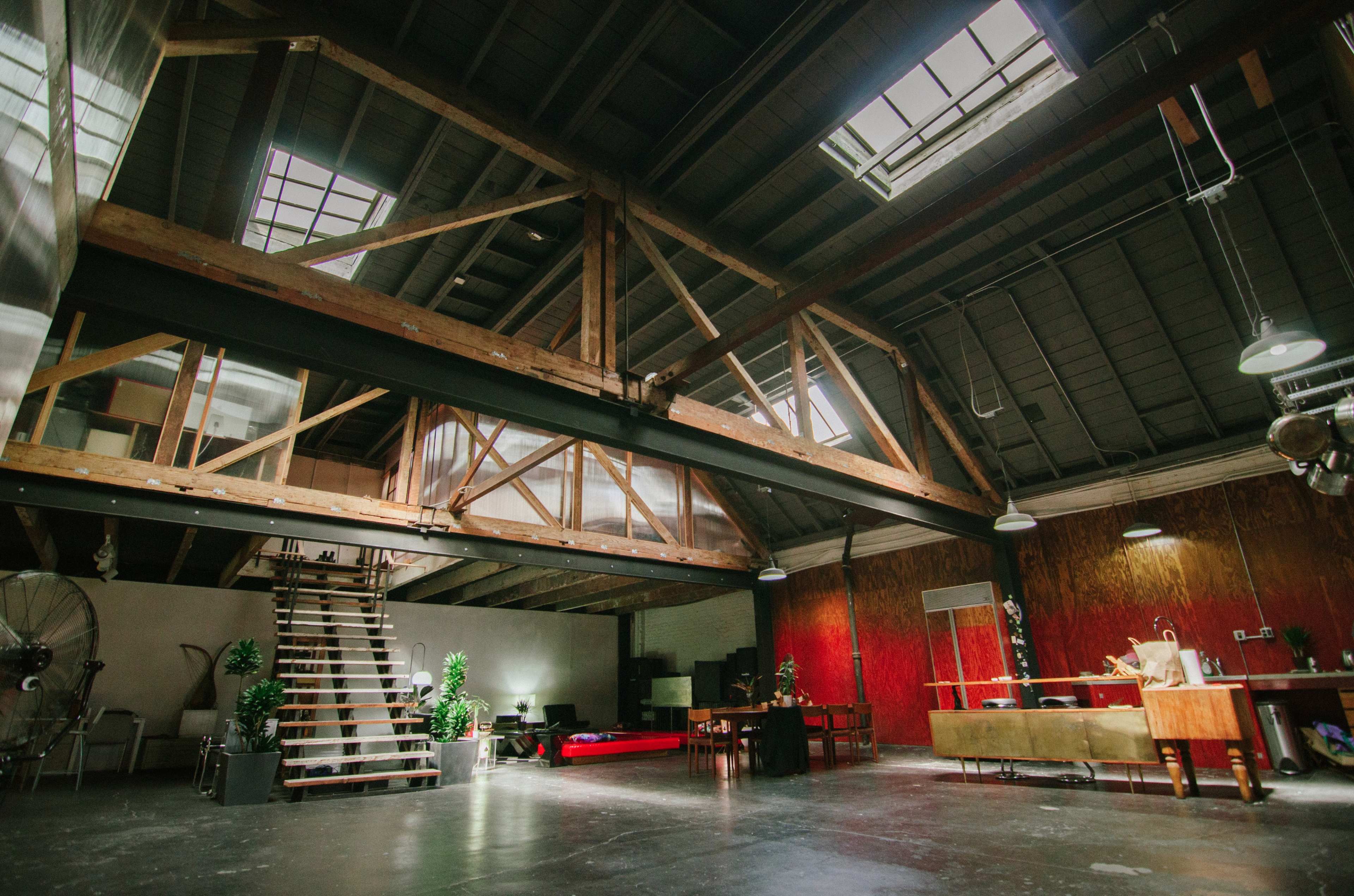 A spacious loft interior with exposed wooden beams, a staircase, and various furniture arrangements in a bright, open environment.