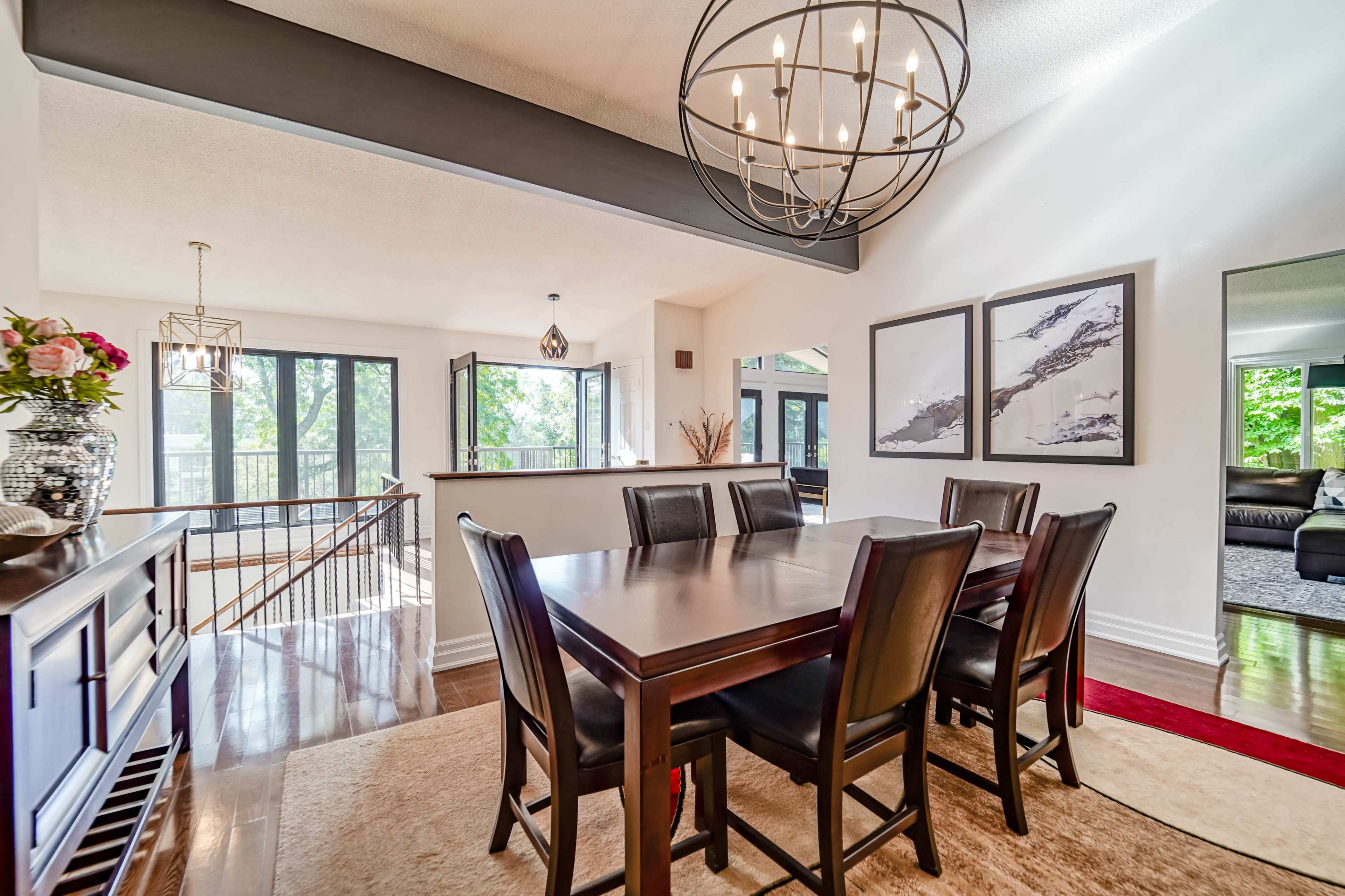 A dining area features a dark wooden table surrounded by black chairs, with large windows and modern decor in the background.