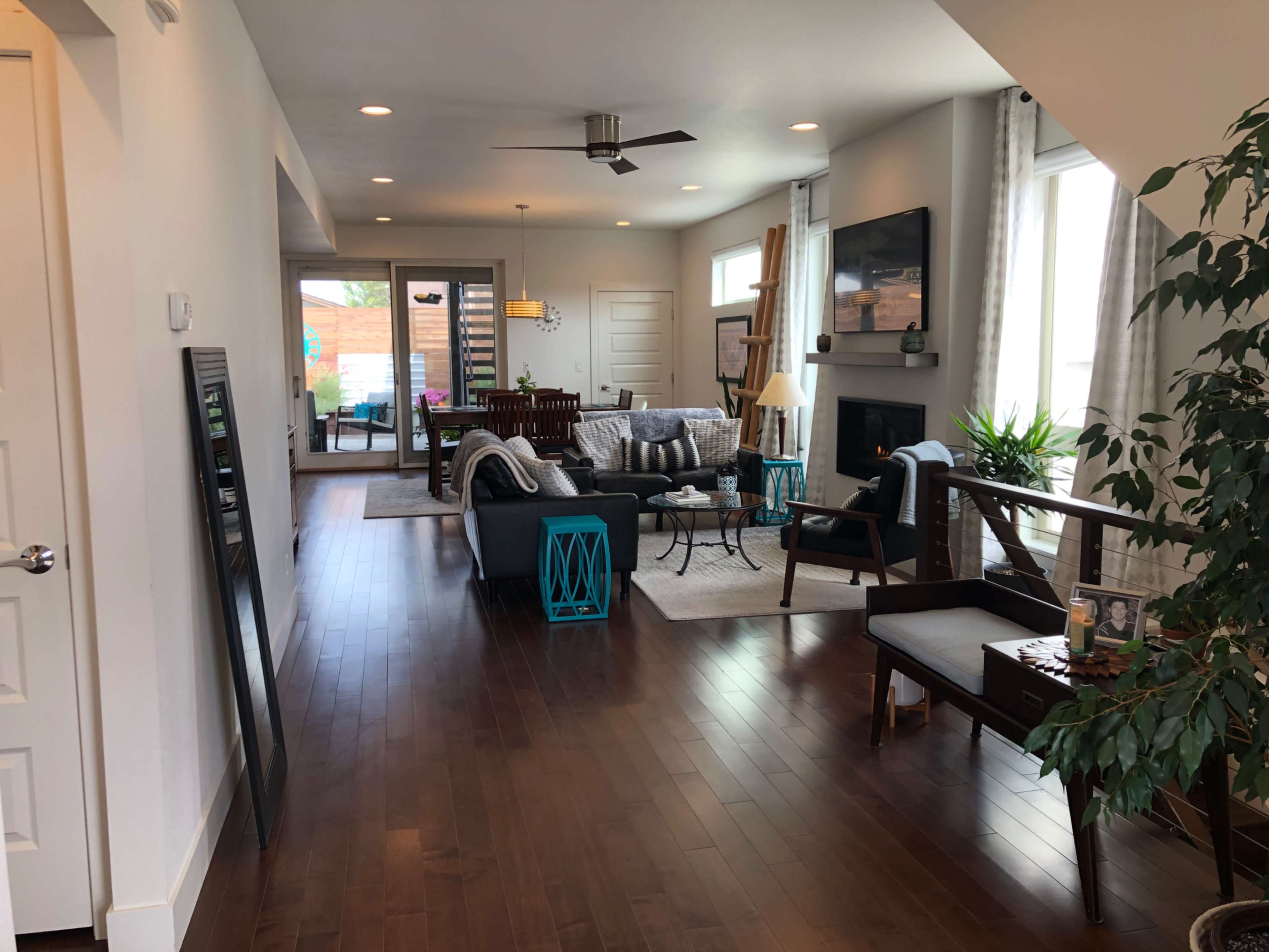 The image shows a spacious and modern living area with hardwood flooring, featuring a seating arrangement, a television, and large windows that provide natural light.