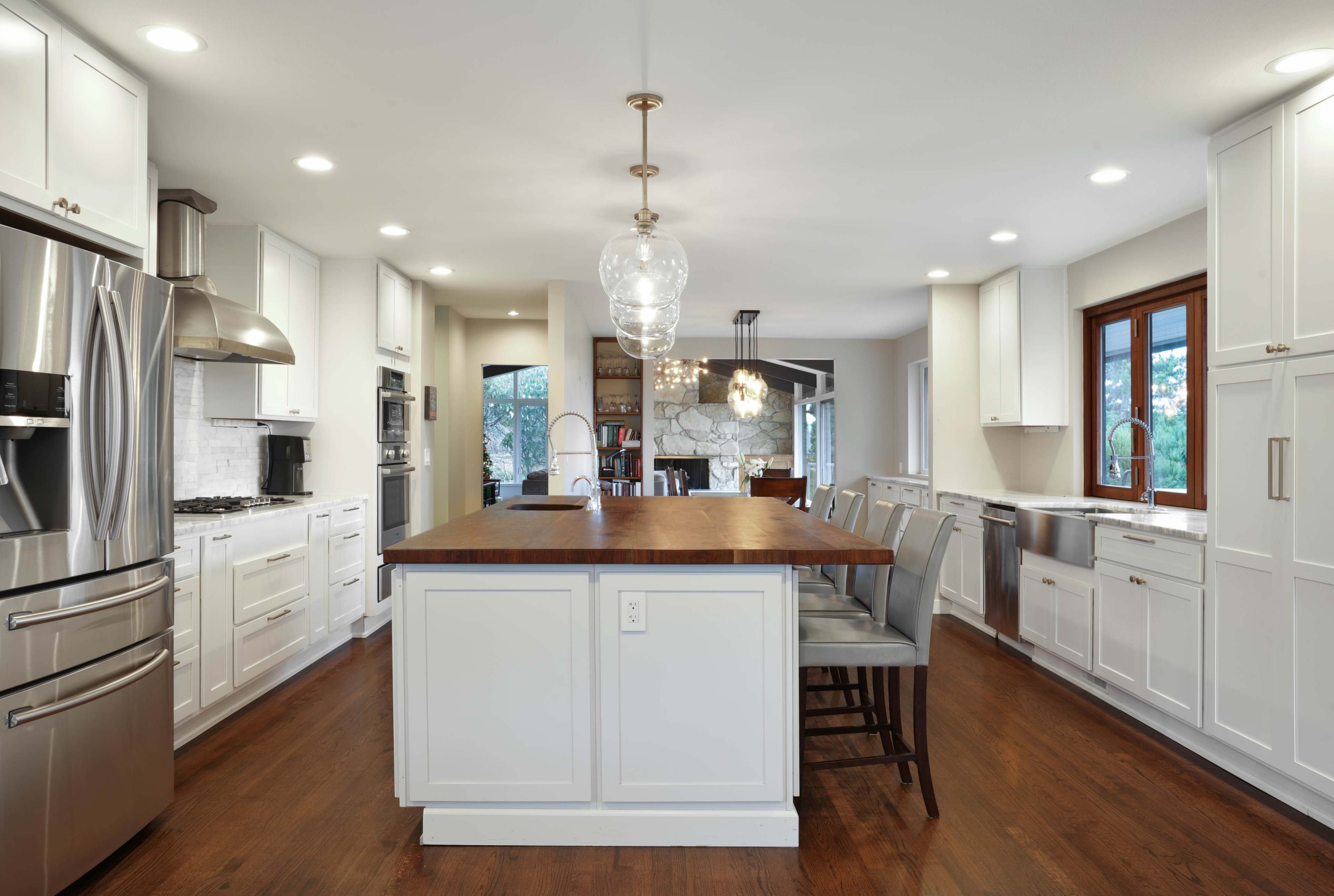 A modern kitchen with white cabinetry, stainless steel appliances, and a central island featuring a wooden countertop and bar seating.