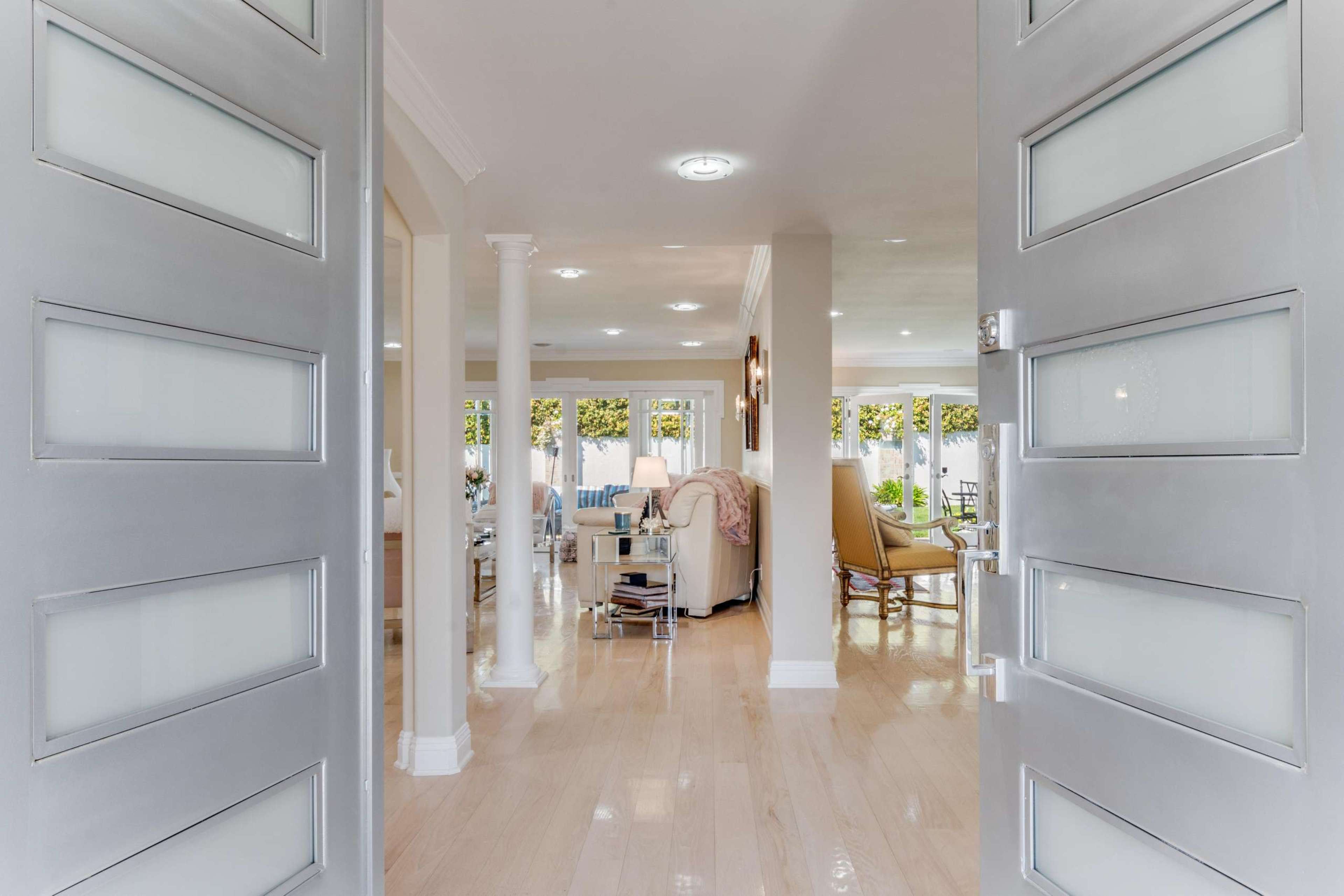 An open entrance with modern glass doors leading into a spacious, bright living area with furniture and large windows.