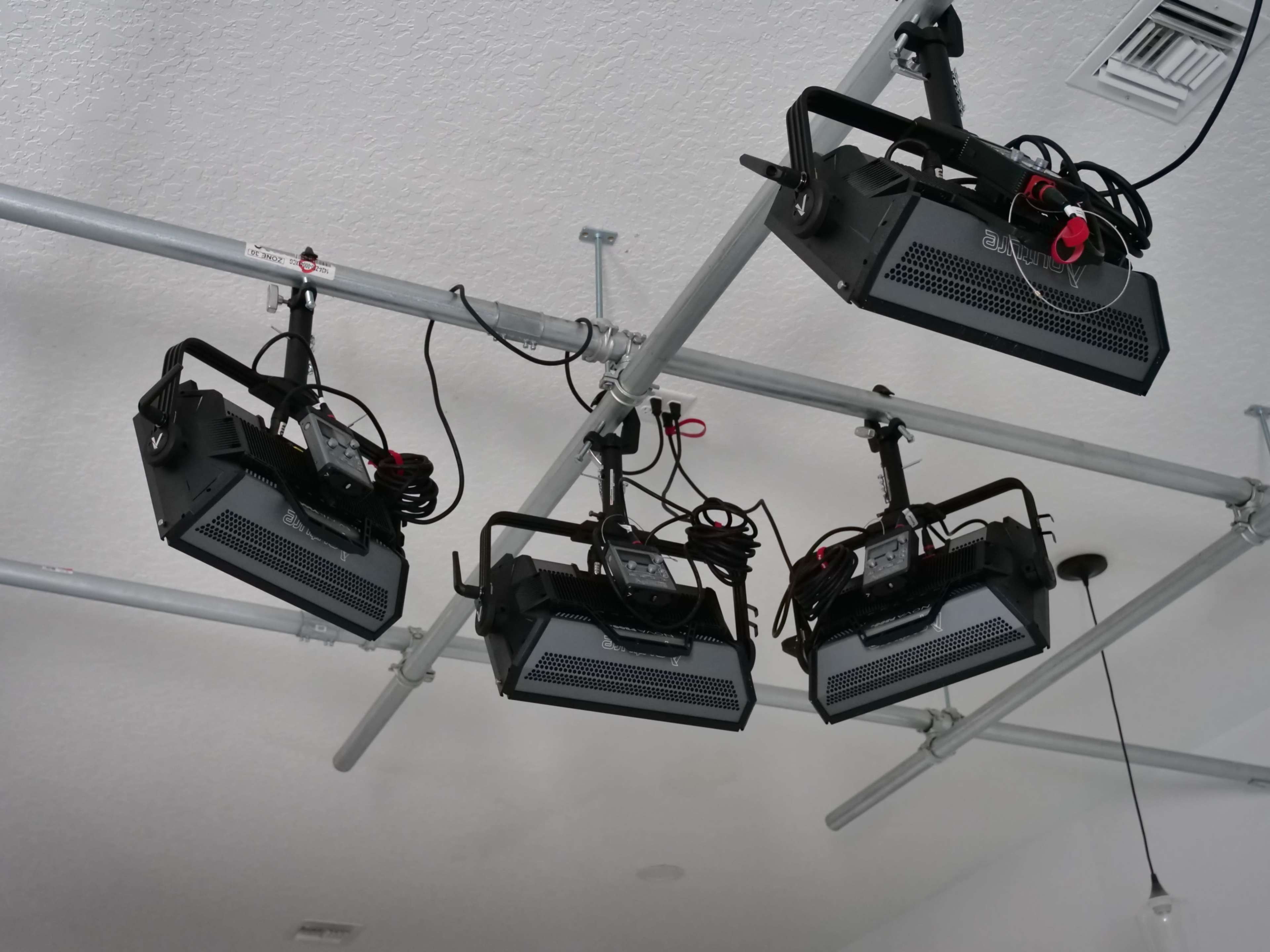 The image shows four studio lights mounted on a metal framing system from the ceiling.
