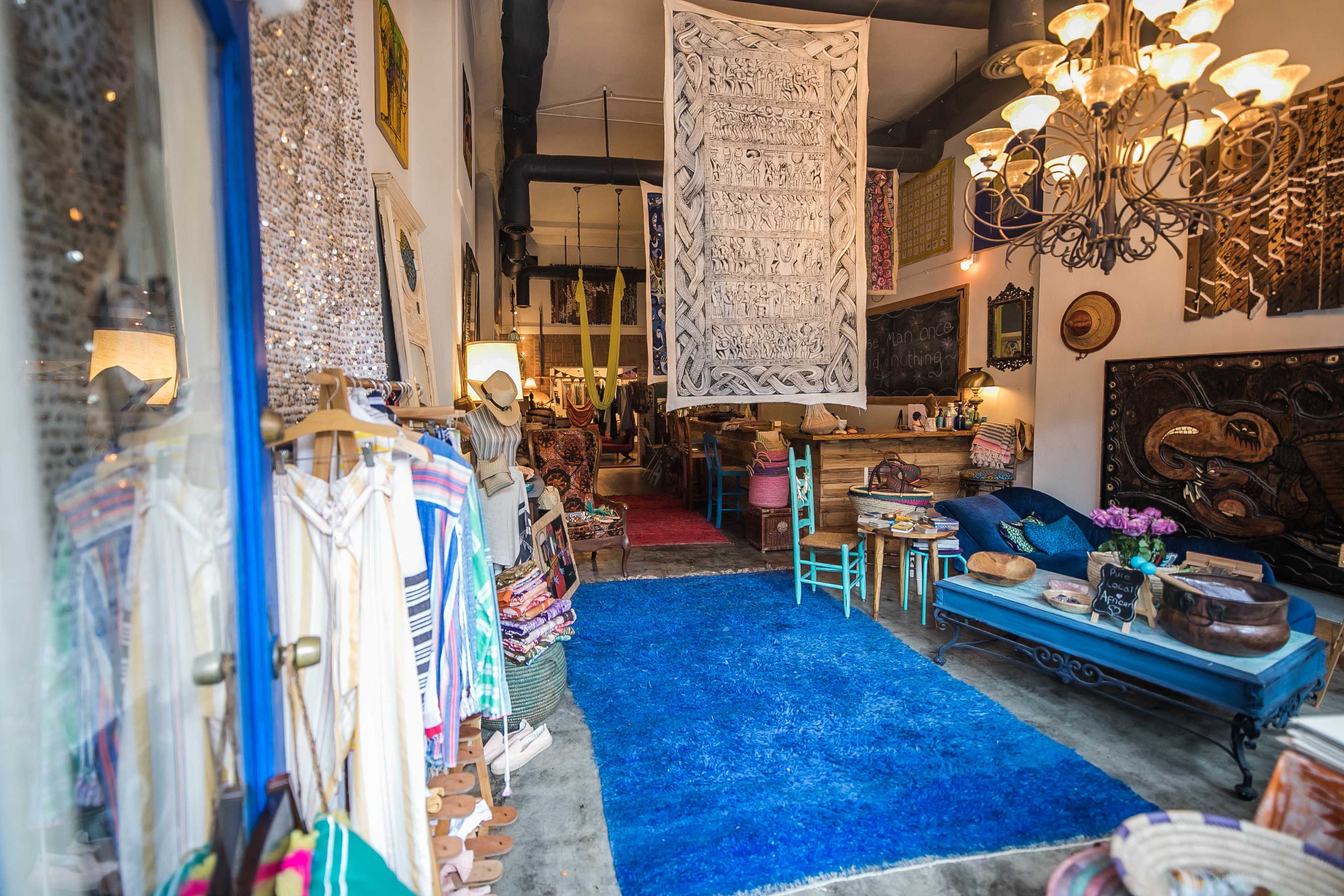 A boutique interior with colorful textiles, a large blue rug, and various decorative items displayed throughout the space.