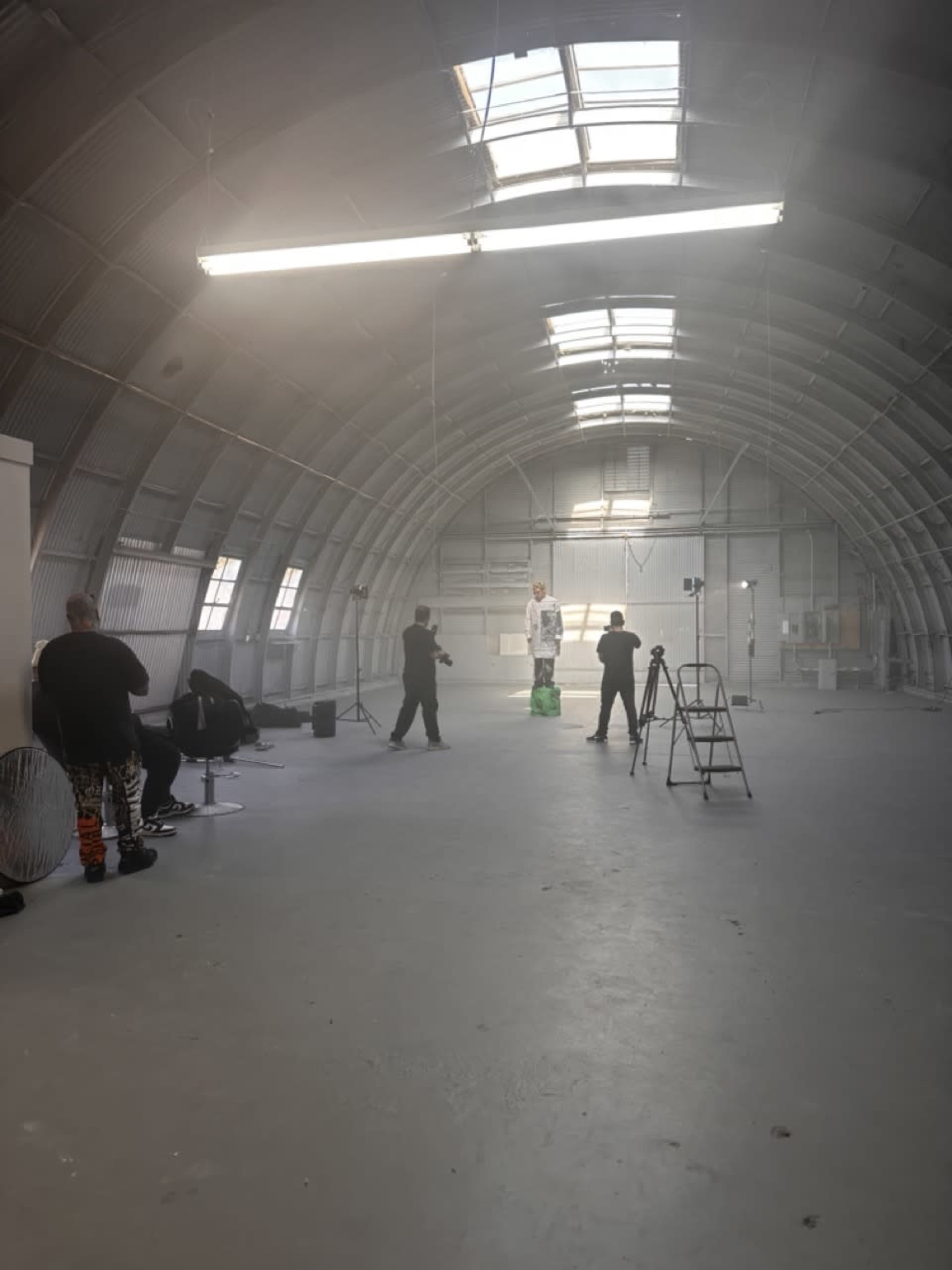 A group of people are setting up a photoshoot in a large, industrial space with a high, arched ceiling.