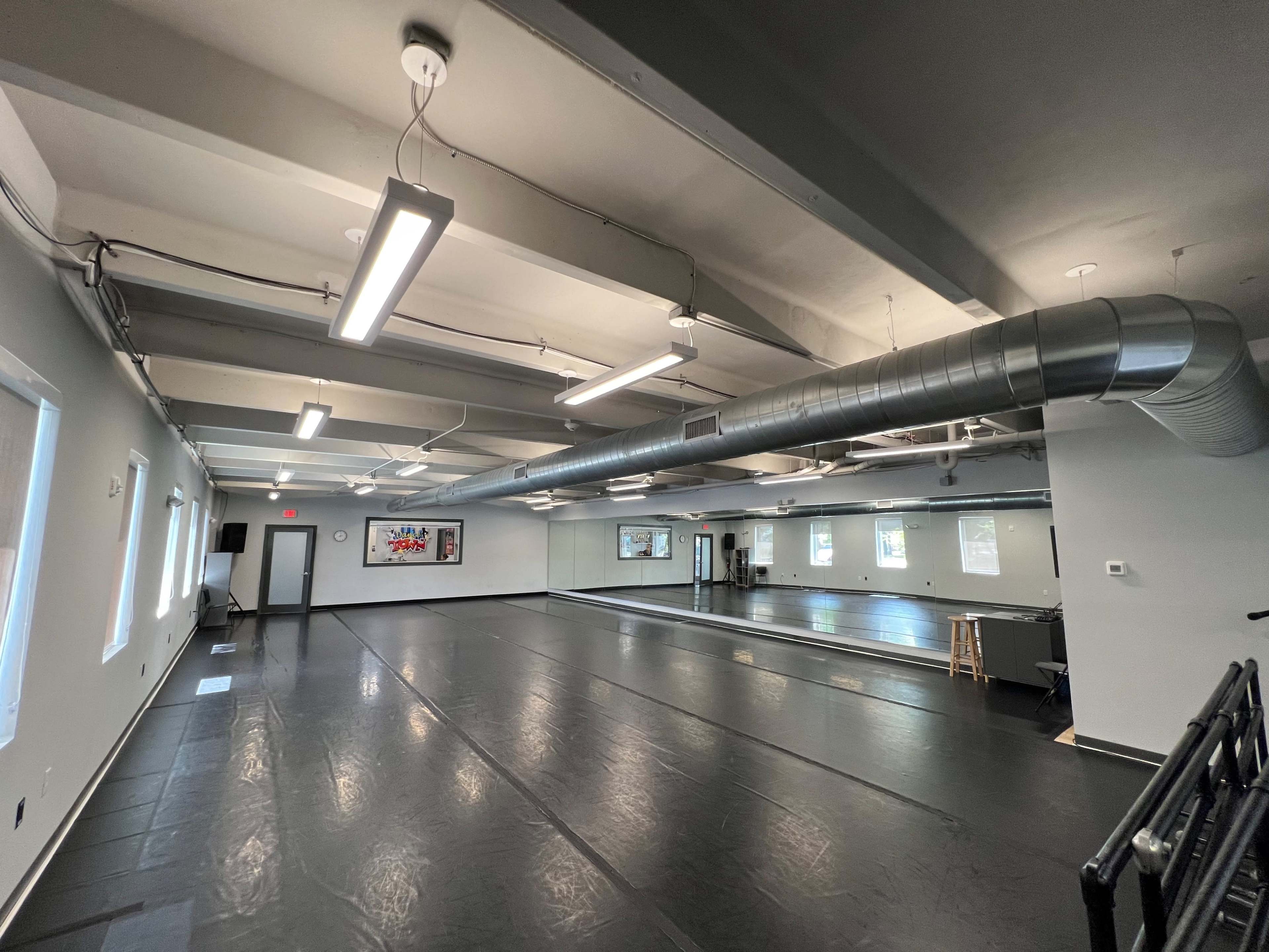 An empty dance studio with mirrored walls, a black floor, and overhead lighting.