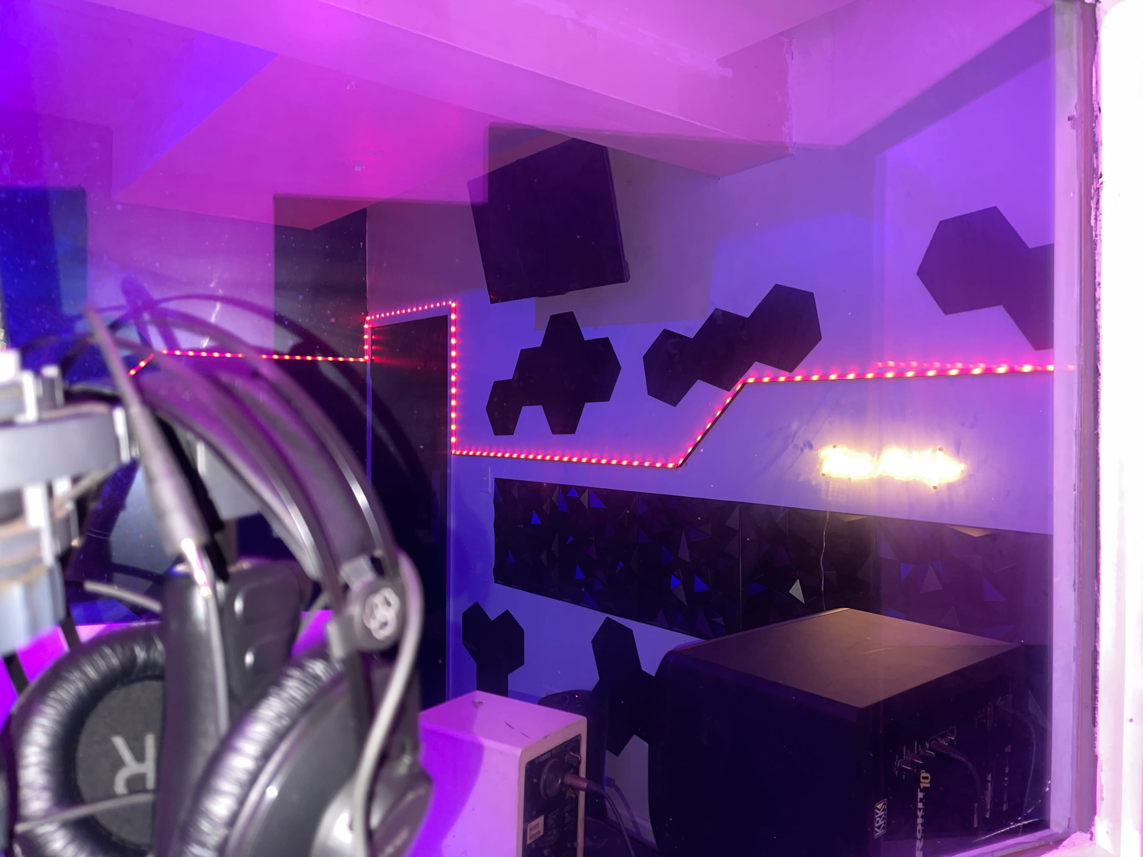 A soundproof music studio with padded walls, LED lighting, and audio equipment visible through a glass window.