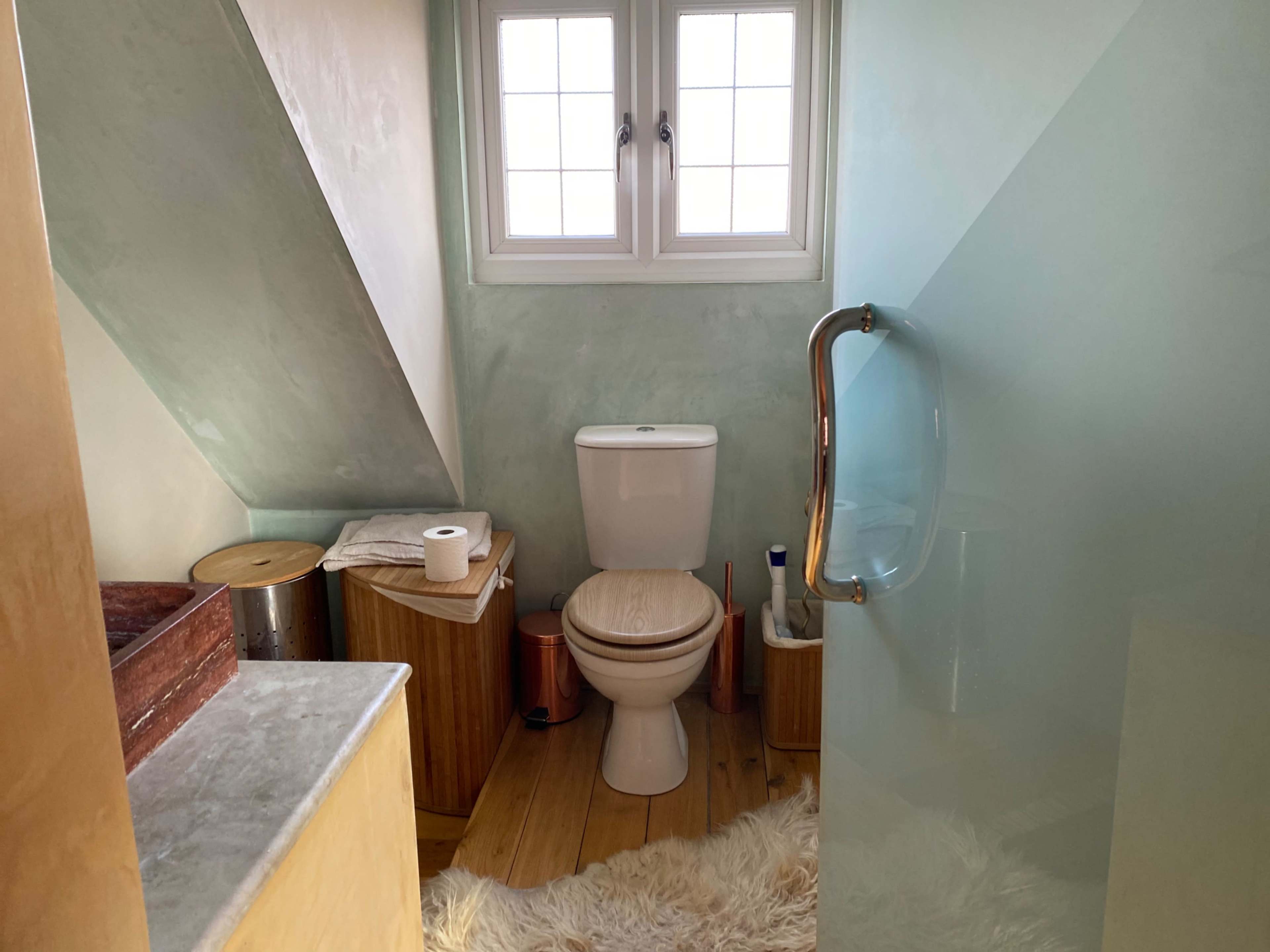 A small bathroom featuring a toilet, a glass shower, and wooden storage units, all under a slanted ceiling.