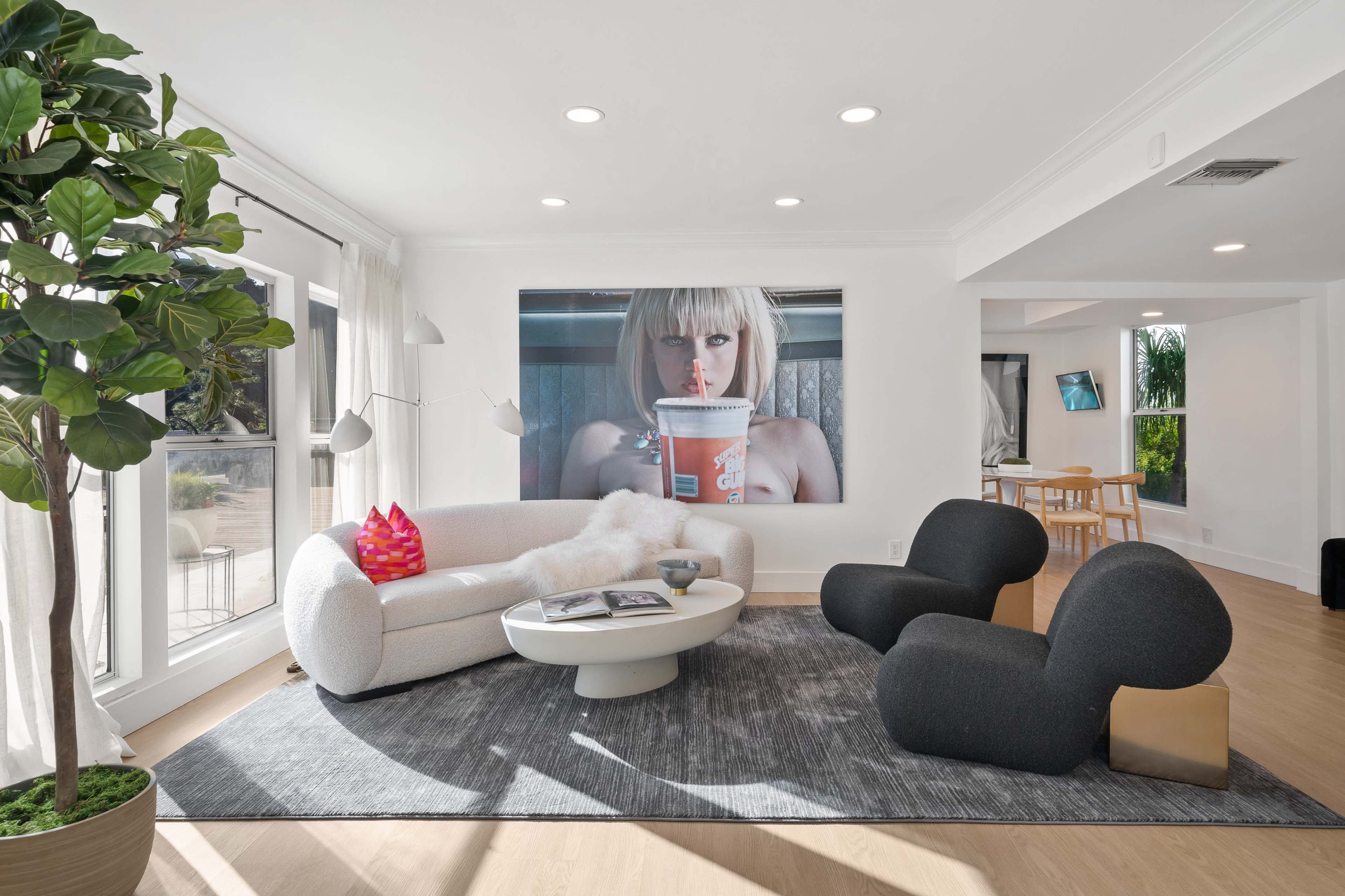 A modern living room with a large wall art piece, a circular coffee table, and unique seating arrangements, surrounded by natural light.