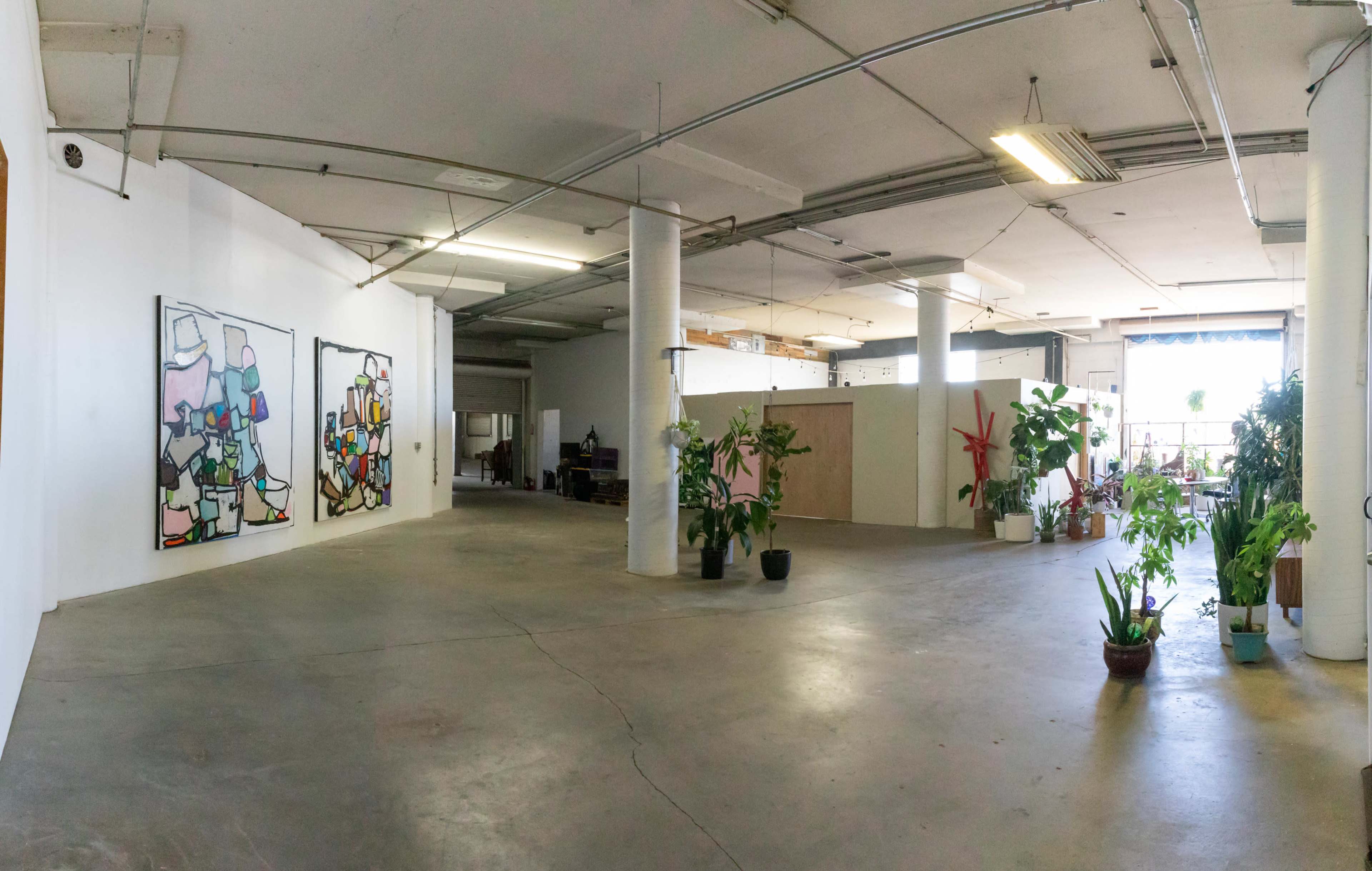 A spacious art gallery with two abstract paintings on the left wall and various potted plants arranged throughout the area.