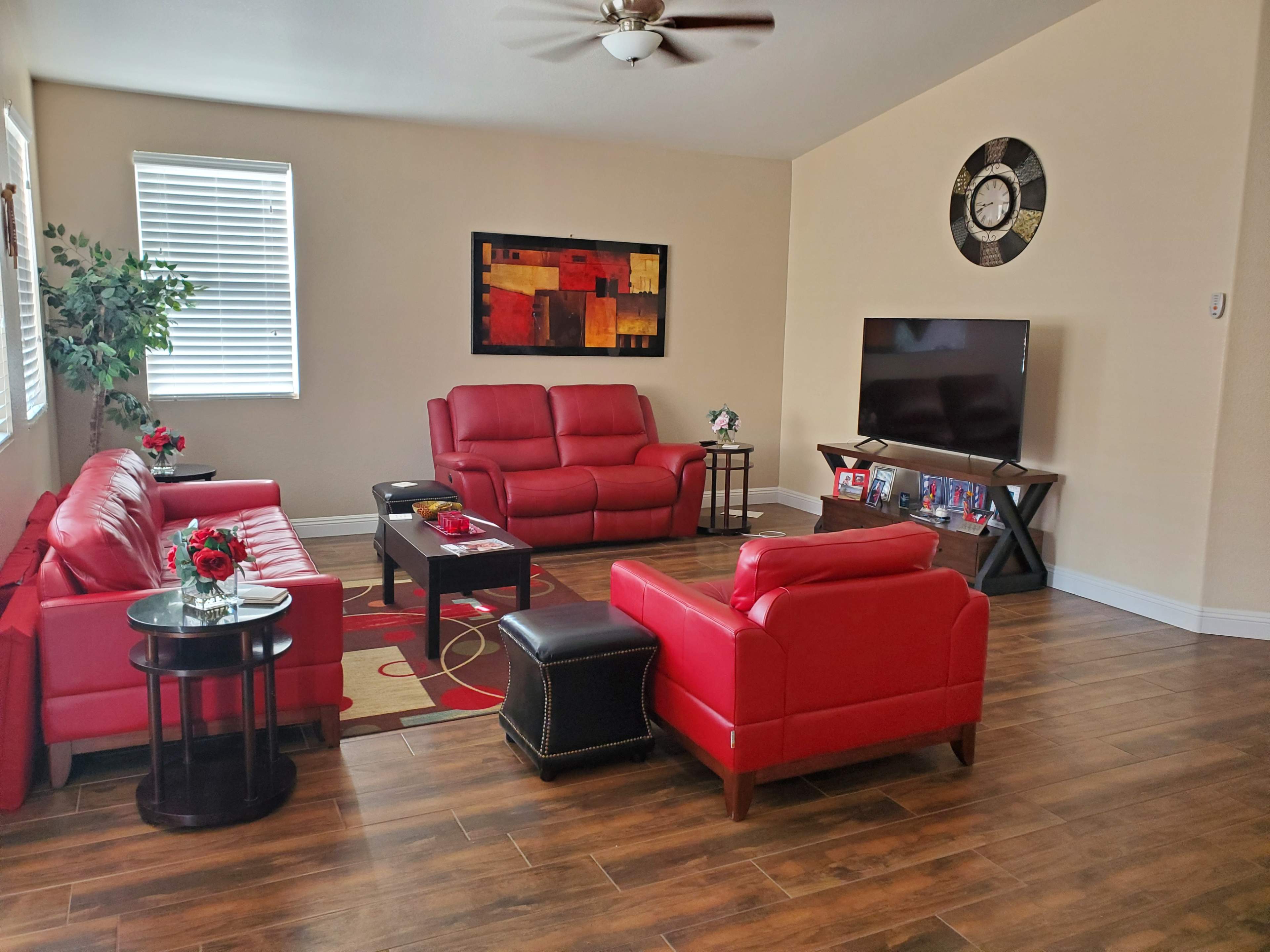 The living room features red leather sofas, a black coffee table, a large television on an entertainment unit, and wall art in a modern style.